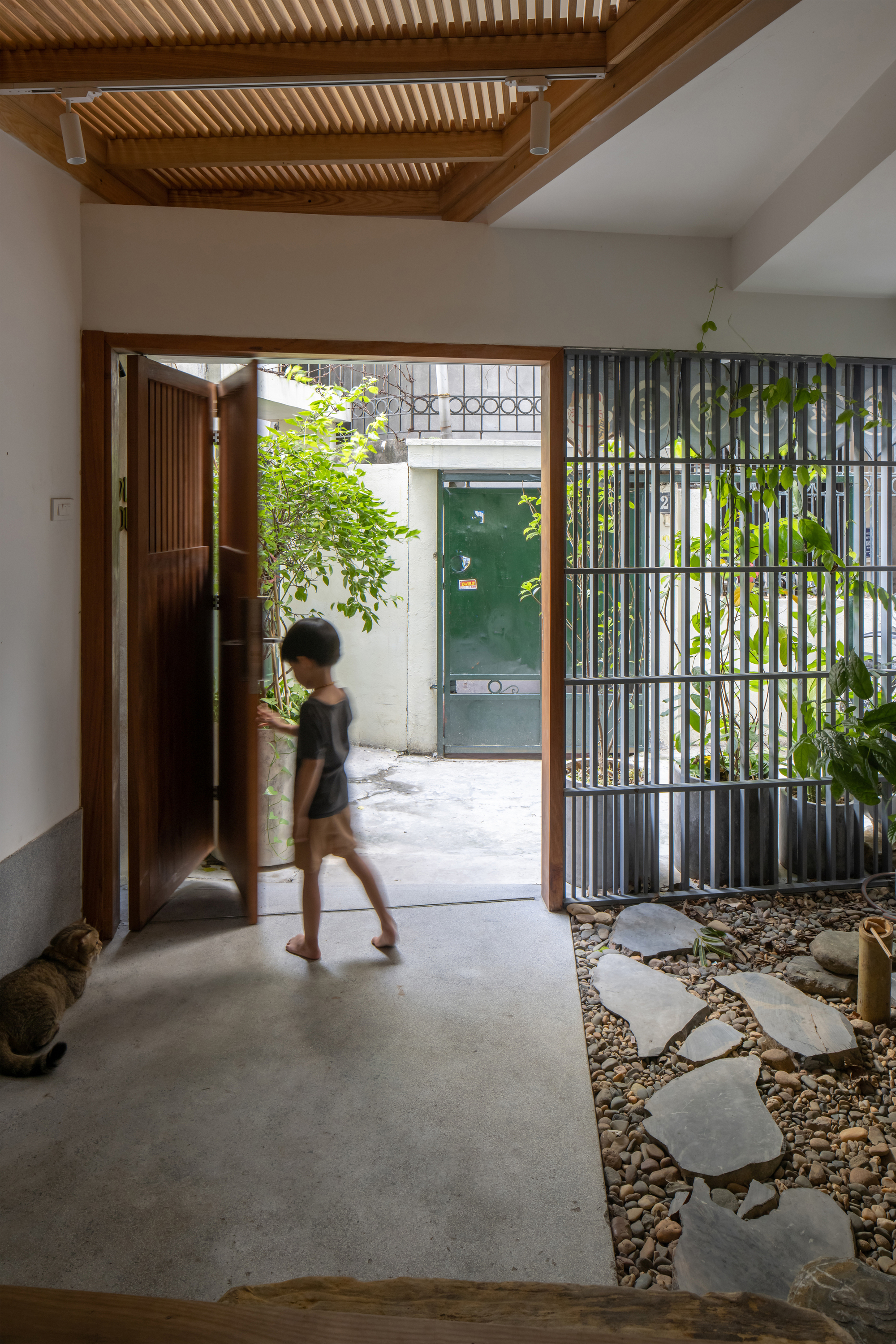 Entry vestibule with folding timber door opening to pebbled courtyard and person walking through in motion