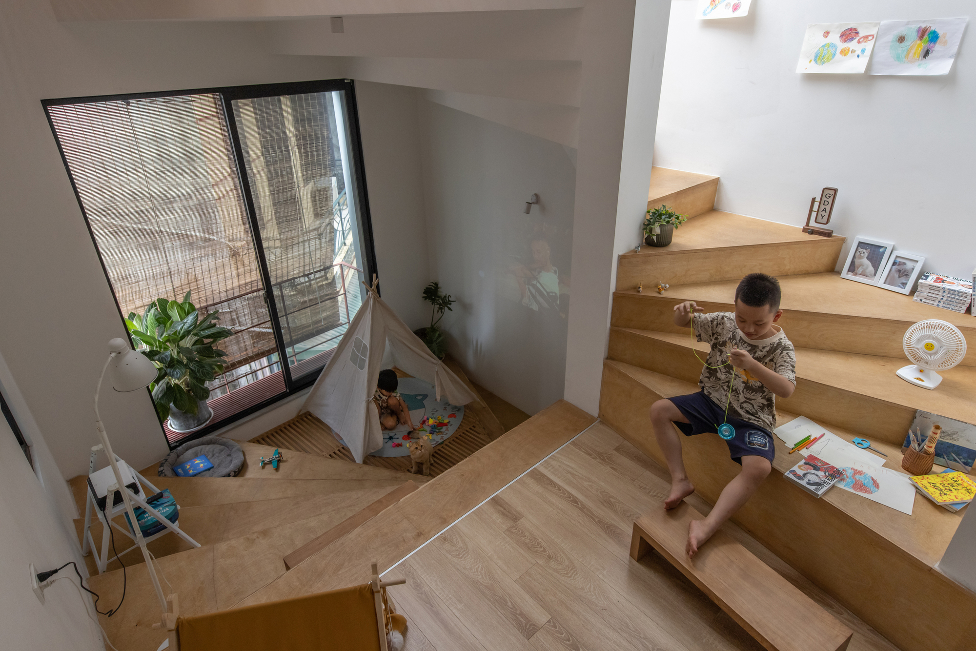 View down to the timber platform where a child sits drawing near a window