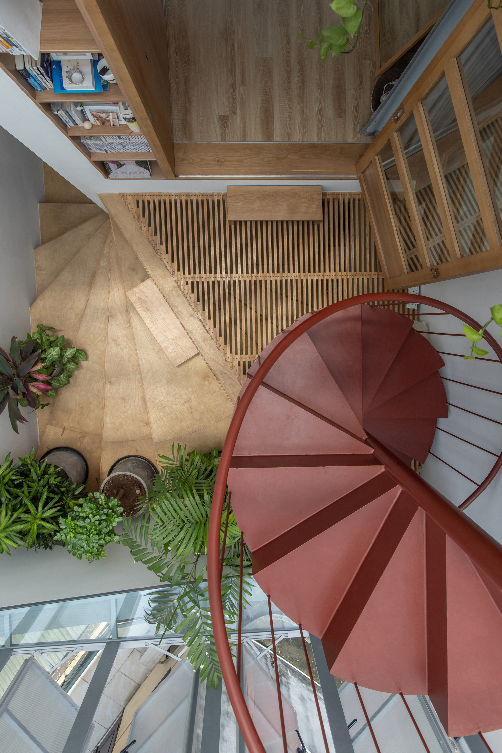 Top-down view of red spiral staircase surrounded by timber screens and potted greenery