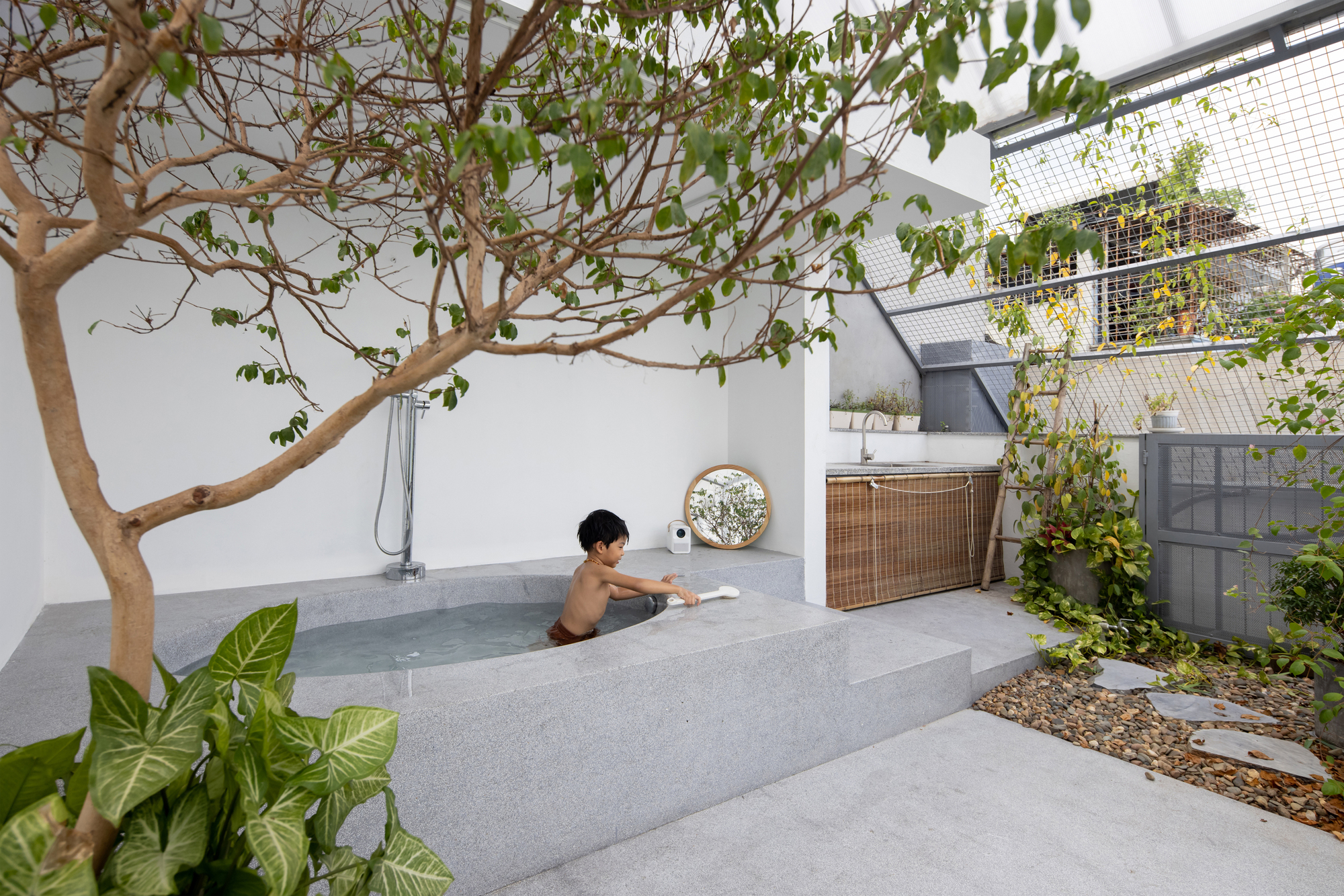 Rooftop terrace with concrete tub, small tree, and person bathing among planted beds