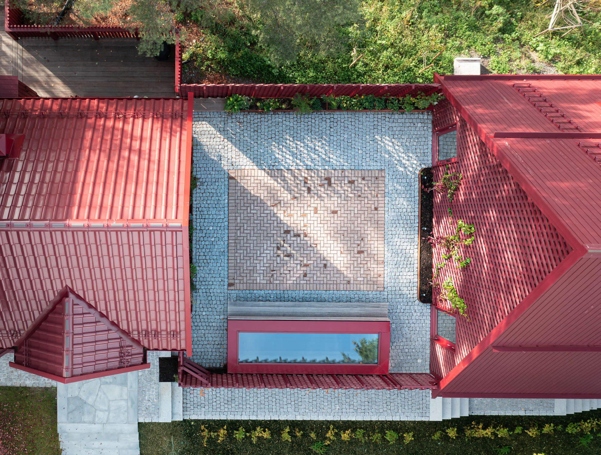 Overhead view of tiled courtyard with chevron pattern framed by red gabled roofs and garden trees