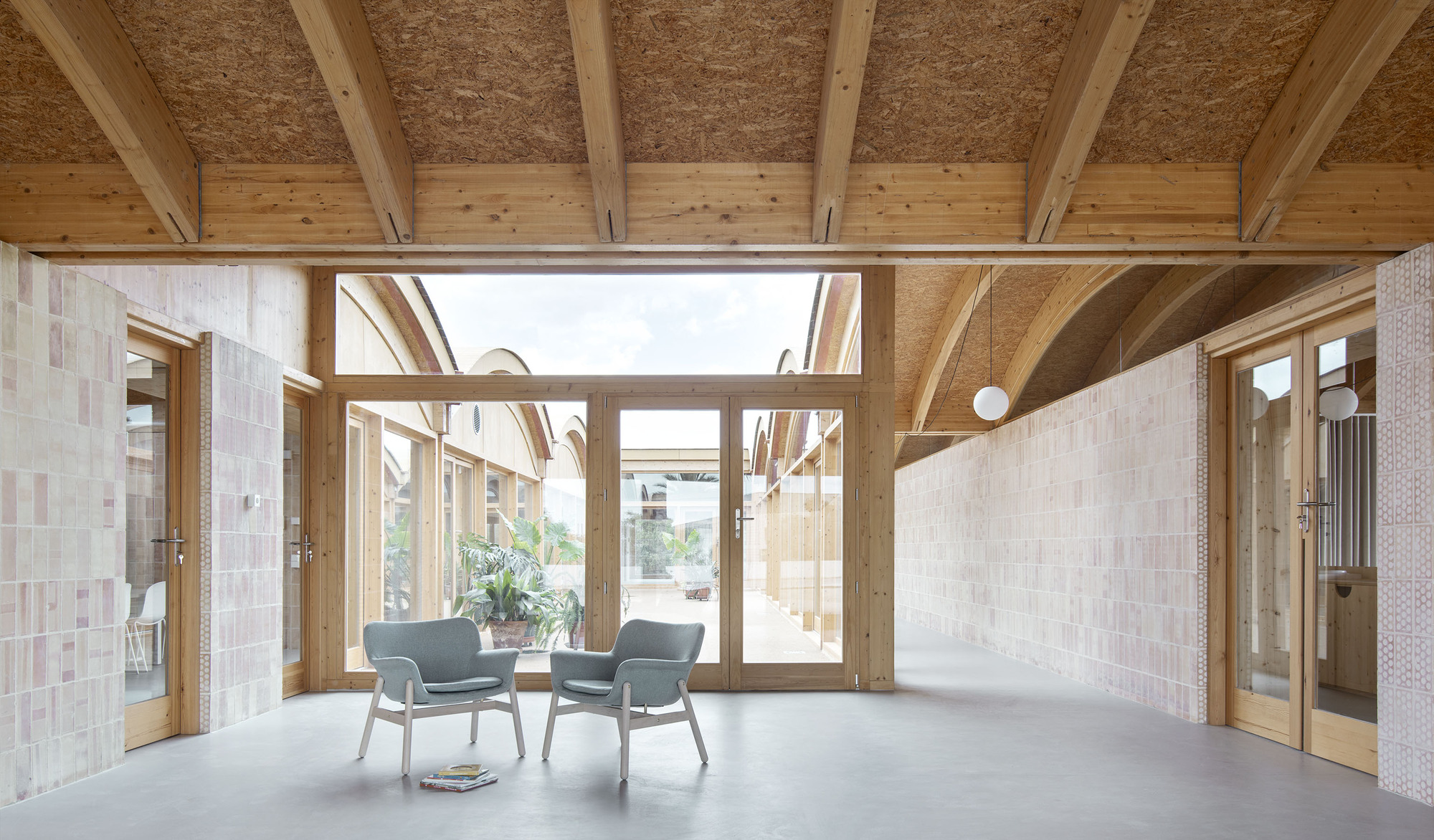 Interior room with exposed timber beams, hempcrete ceiling panels, and glazed doors opening to a courtyard