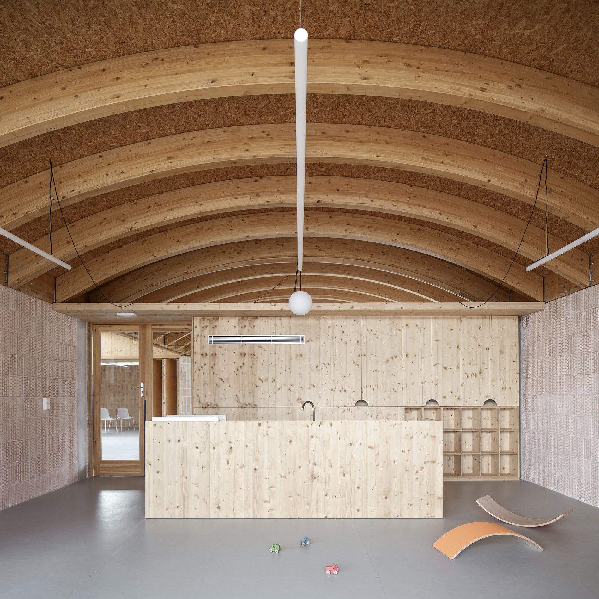 Interior space with curved laminated timber arches and a plywood island beneath suspended pendant lighting