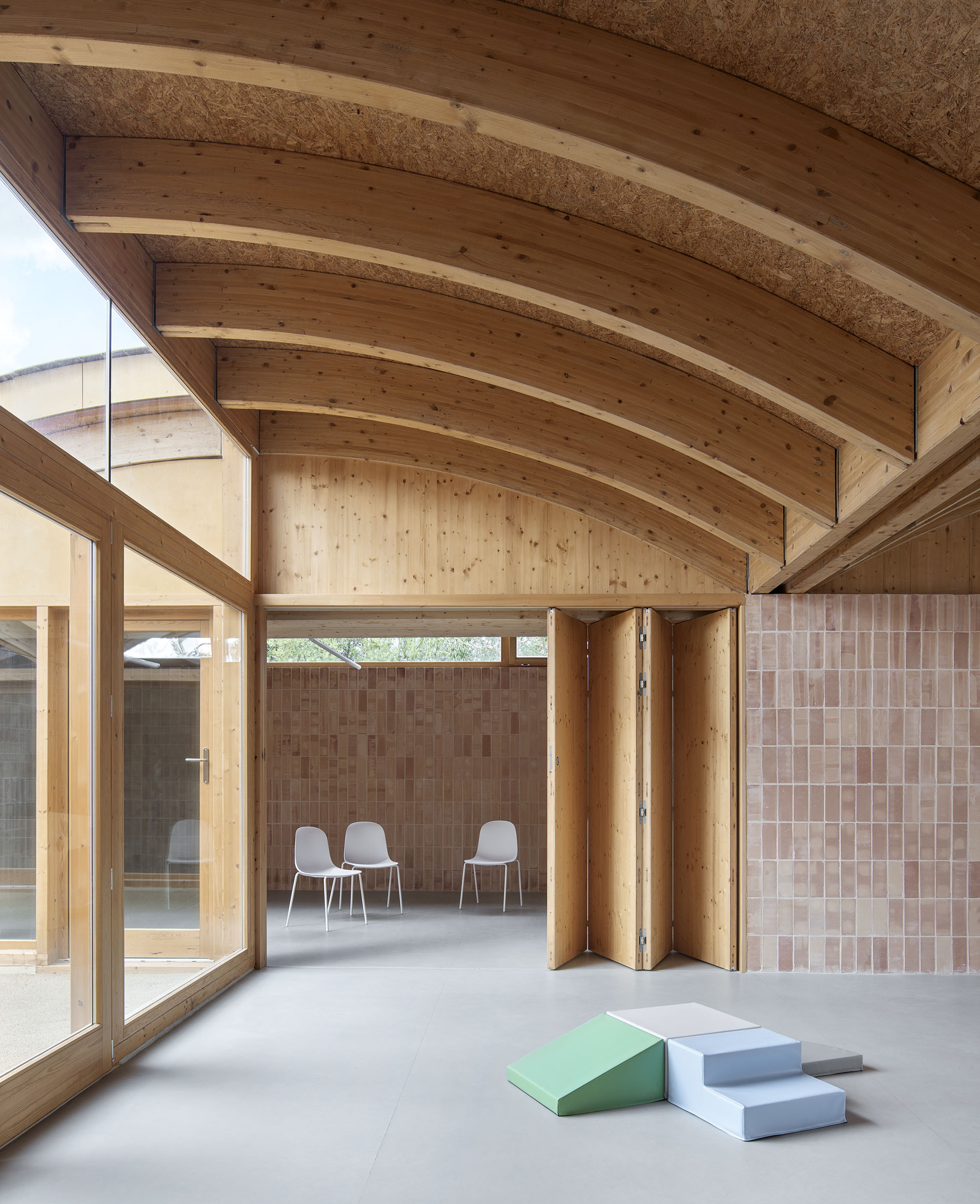 Corner view showing curved timber rafters, folding timber screens, and foam play blocks on the floor