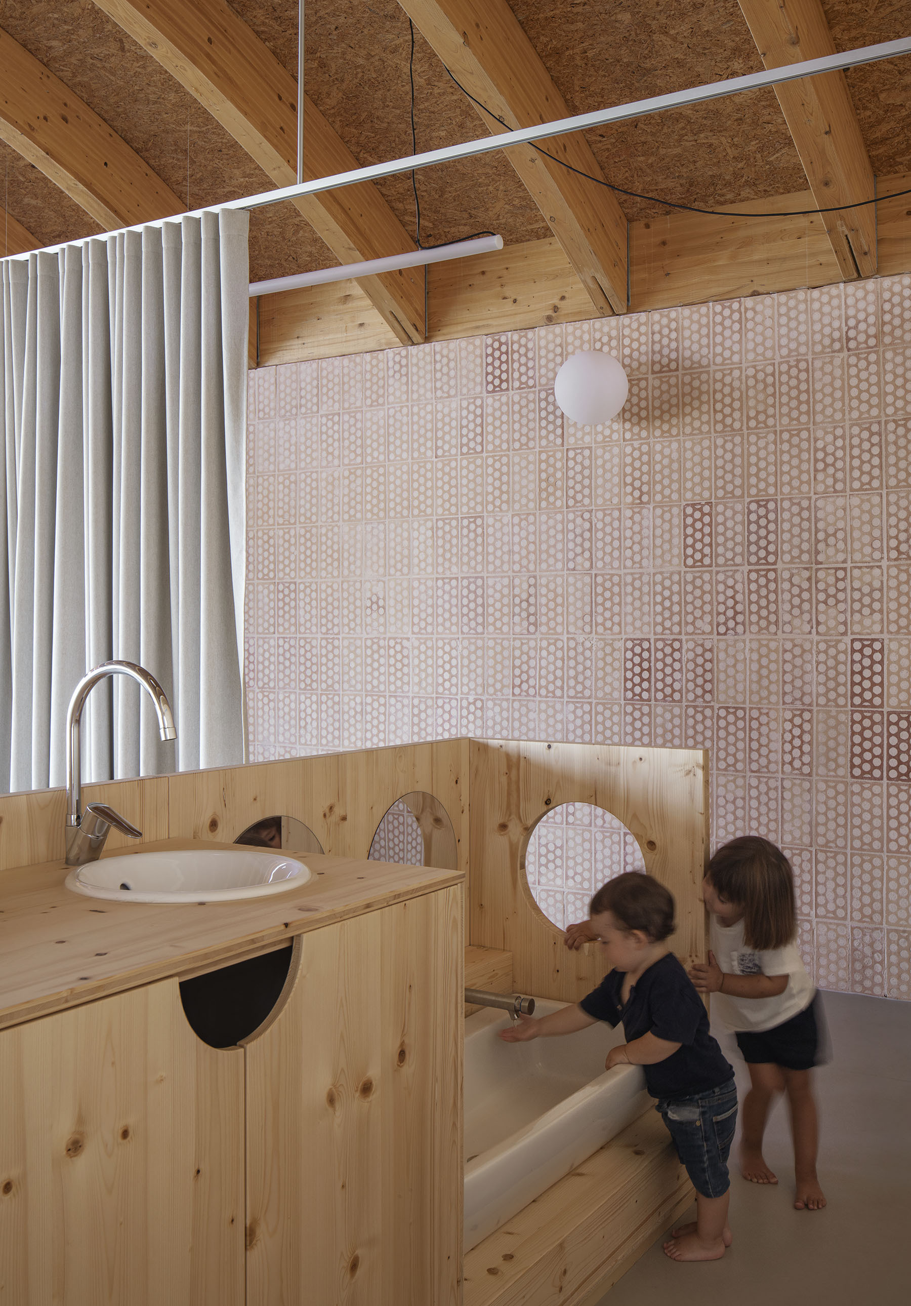 Timber bathroom vanity with circular mirrors and children using the facilities beneath a perforated panel wall