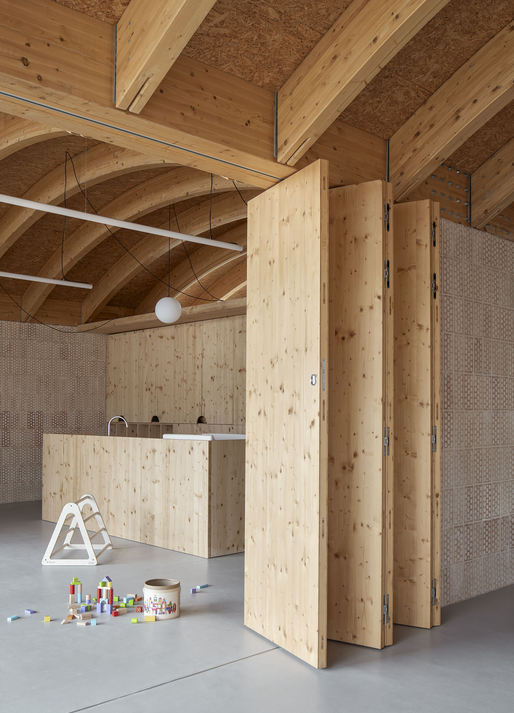 Interior space showing folding timber partitions beneath vaulted wooden ceiling with scattered toys on the floor