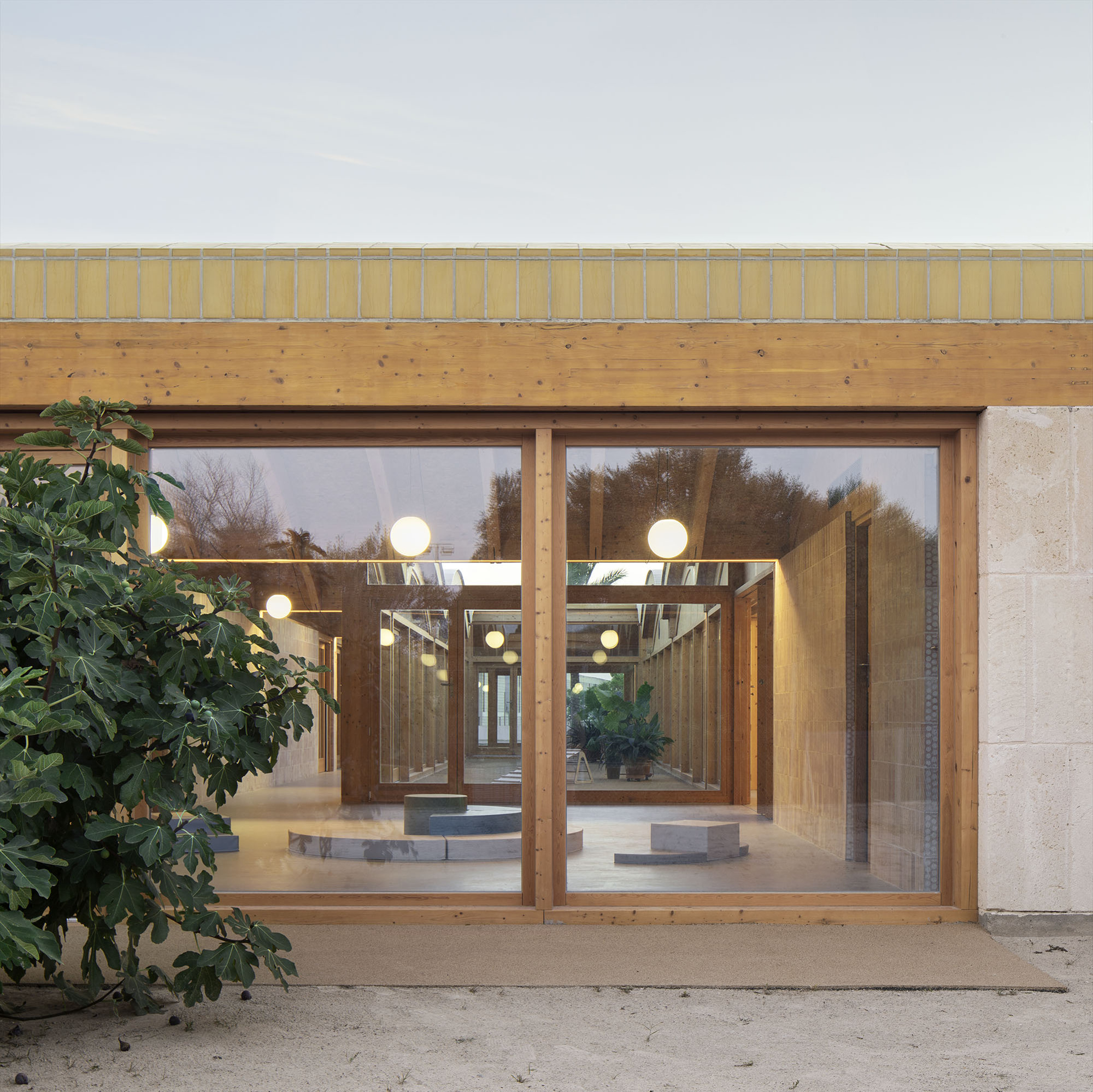Glazed facade with timber frames revealing illuminated interior and suspended globe lights at dusk
