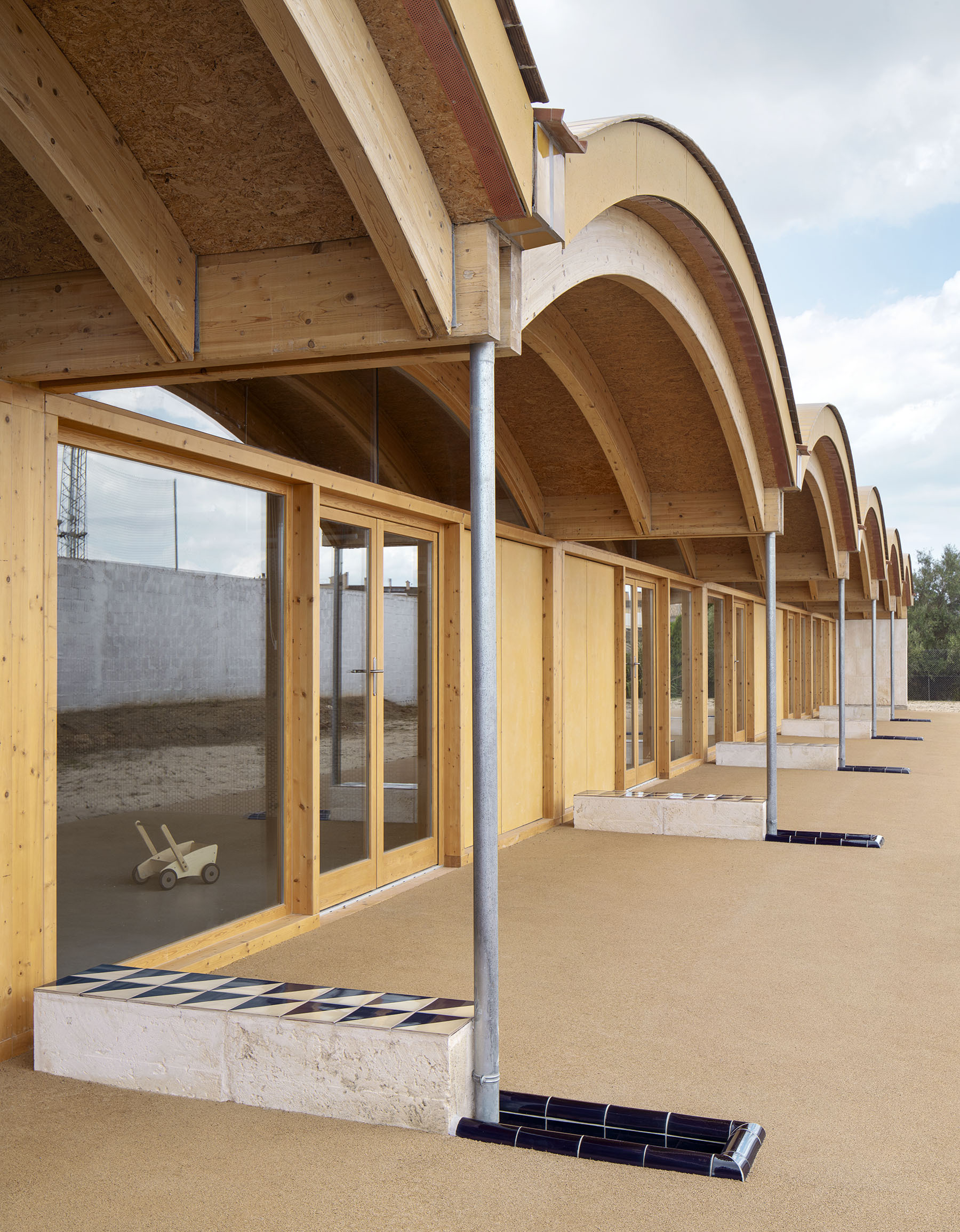 Angled view of the covered walkway showing timber columns and arched vaults under a partly cloudy sky