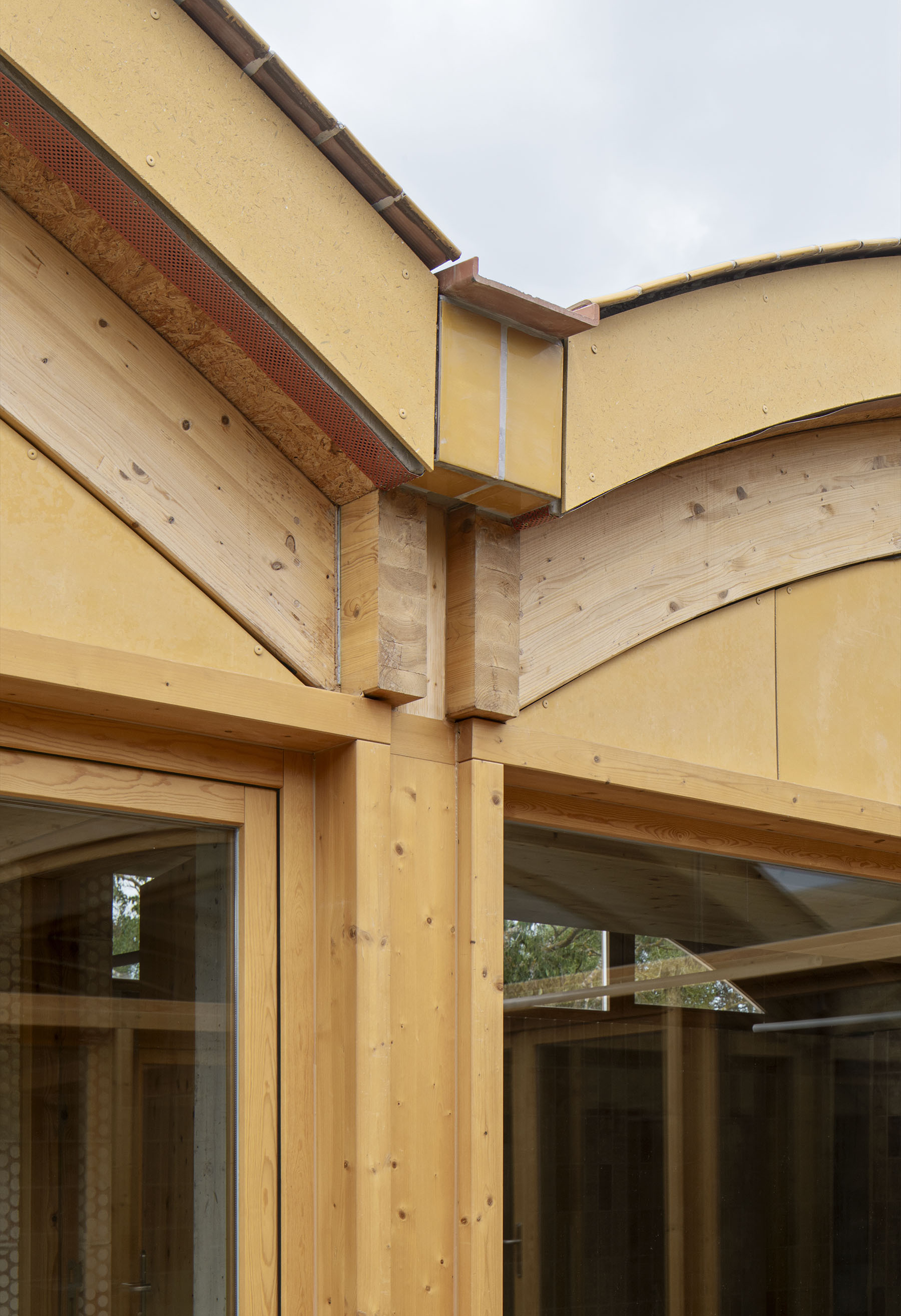 Detail of timber post and beam junction with yellow hempcrete panels and exposed laminated timber arches