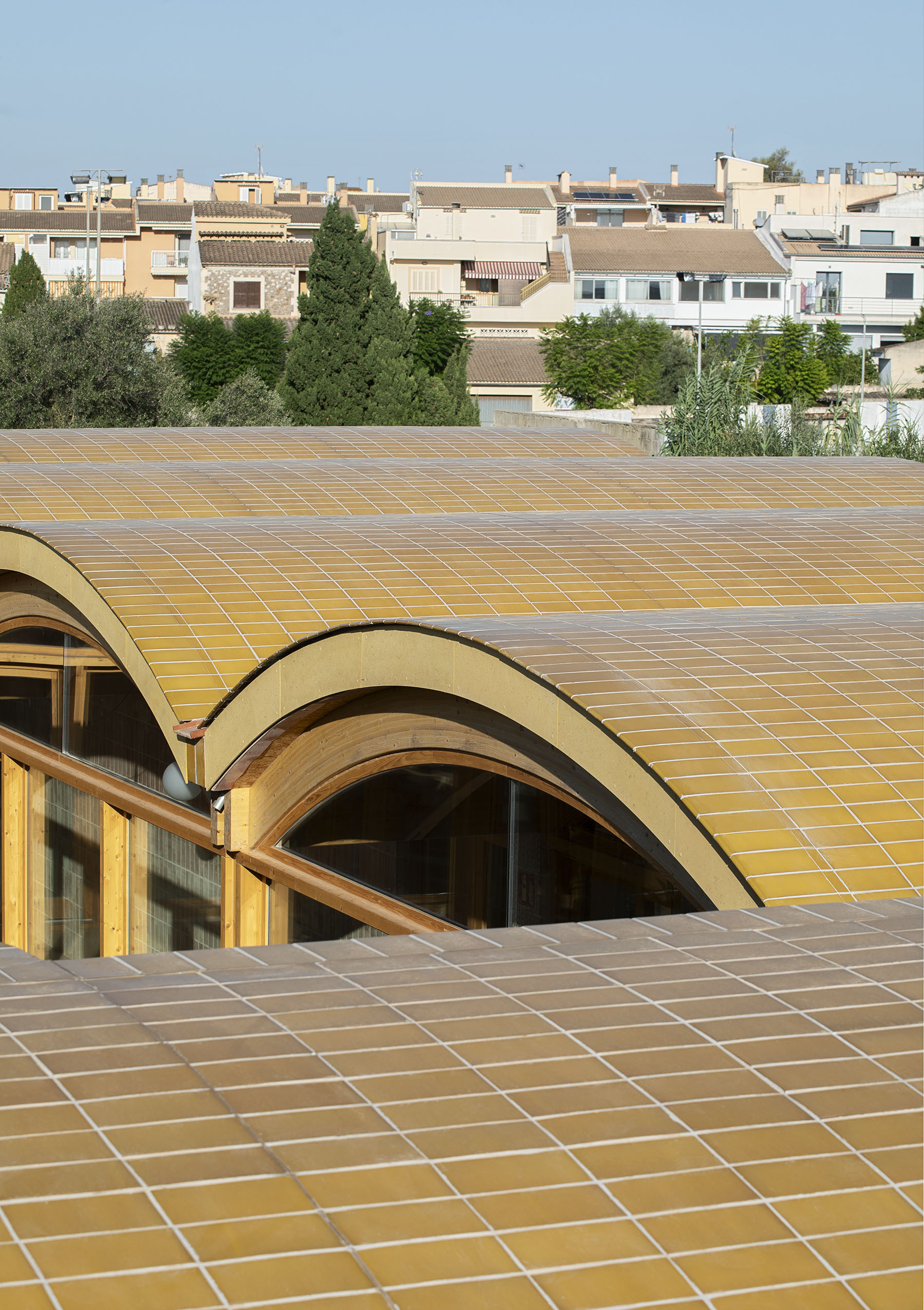 Undulating tiled roof in ochre yellow ceramic with residential buildings visible in the background