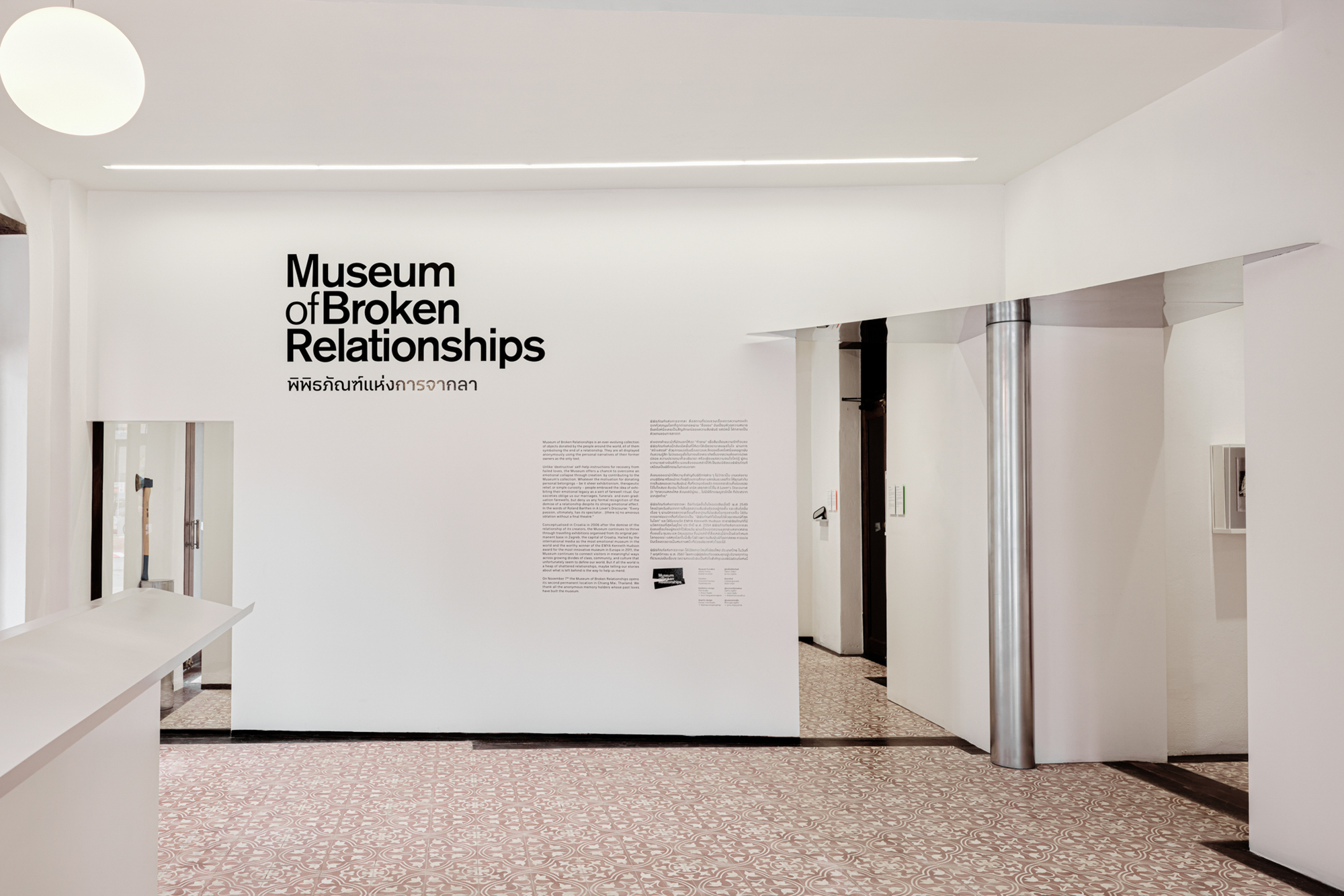 Exhibition entrance wall with black typography and descriptive text panels above terrazzo flooring