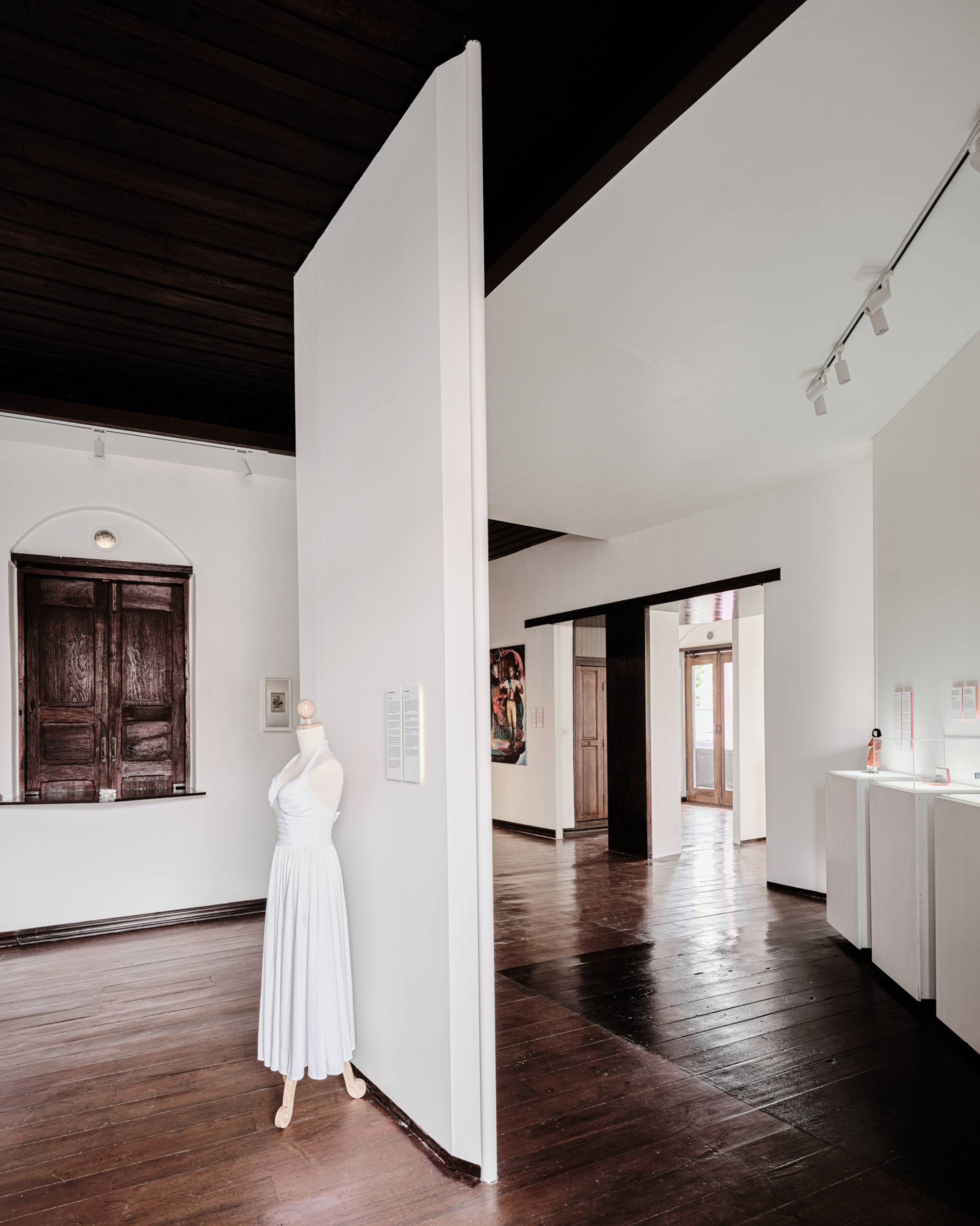 Freestanding white partition wall with a dress form displayed and dark timber ceiling above