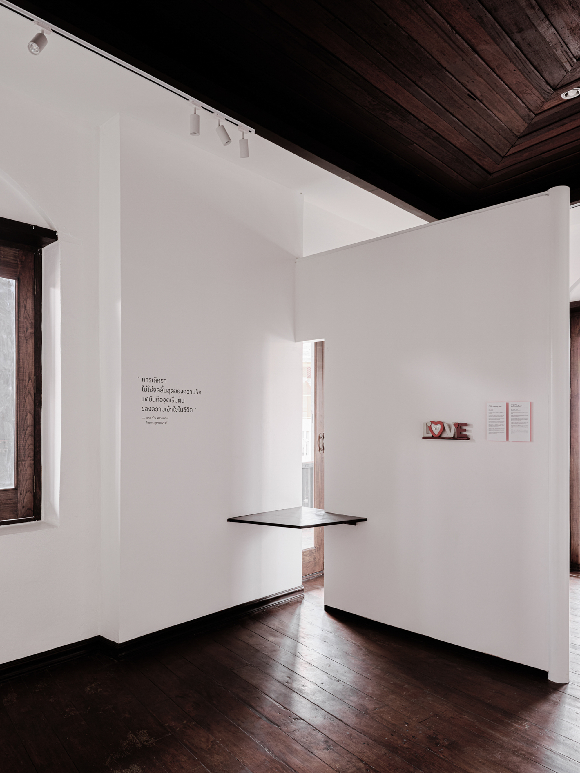 Narrow vertical opening in a white partition wall with a floating shelf and dark flooring