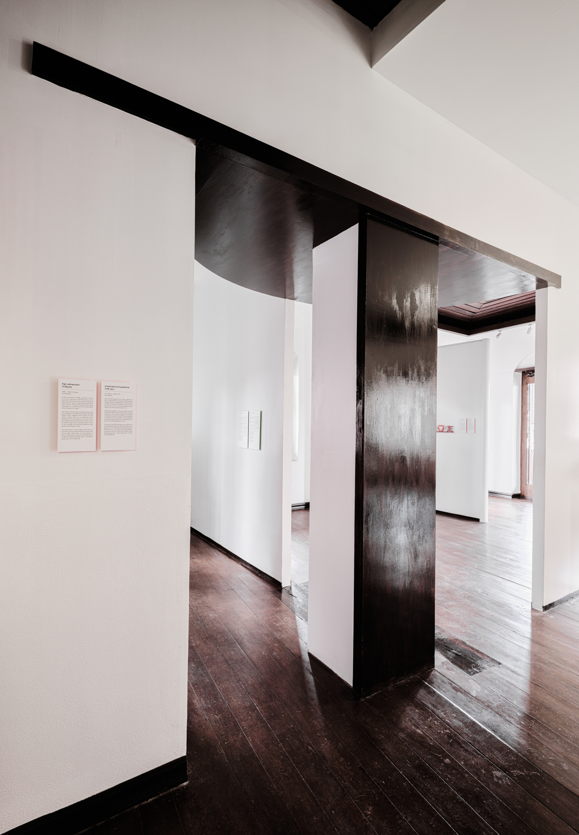 Blackened steel structural column framing a sequence of gallery doorways with dark timber floors
