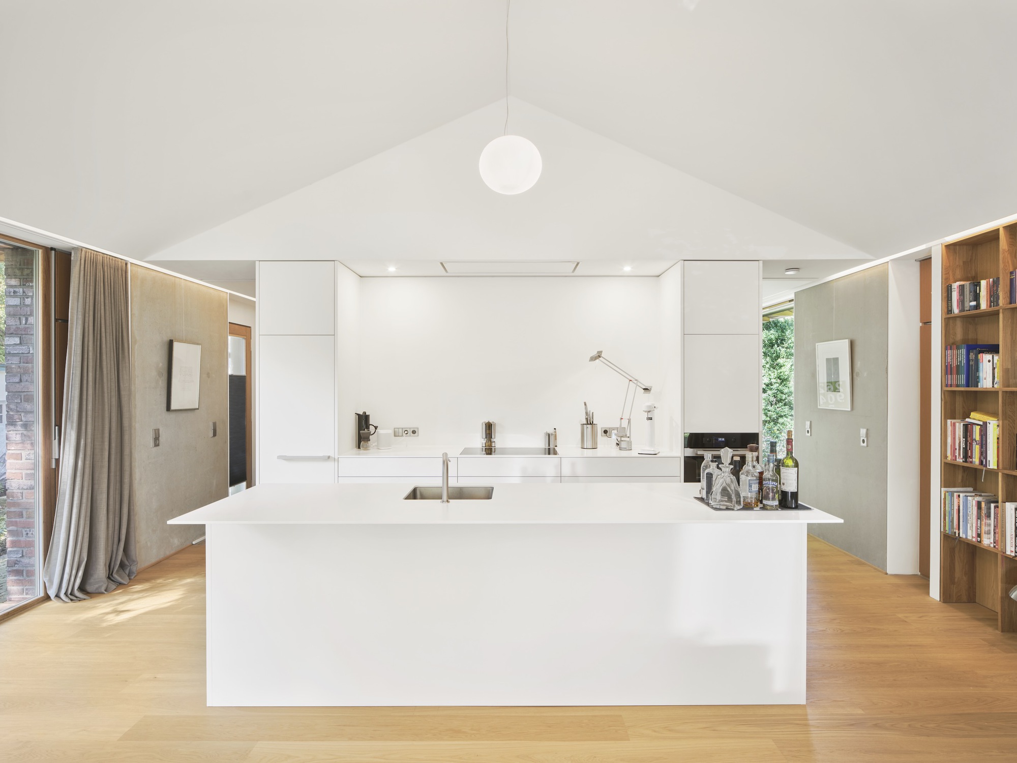White kitchen island beneath vaulted ceiling with spherical pendant light and continuous perimeter slot lighting