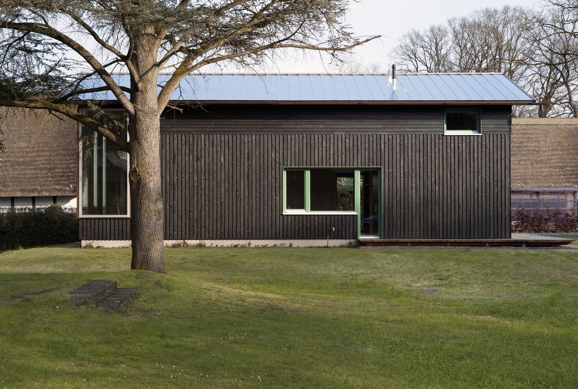 Corrugated timber facade with standing seam metal roof and mature deciduous tree in winter lawn