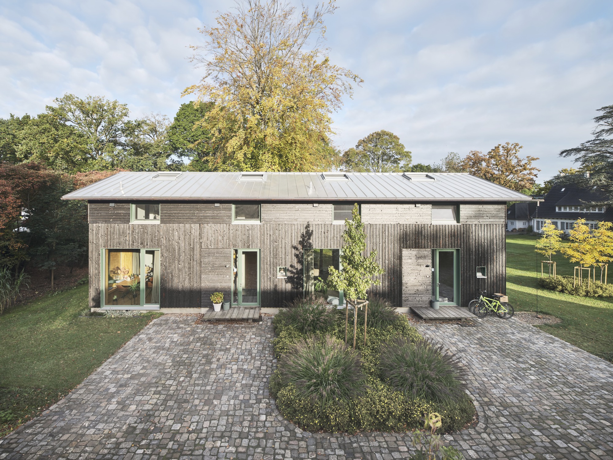 Entrance facade with corrugated timber cladding and planted cobblestone courtyard at dusk