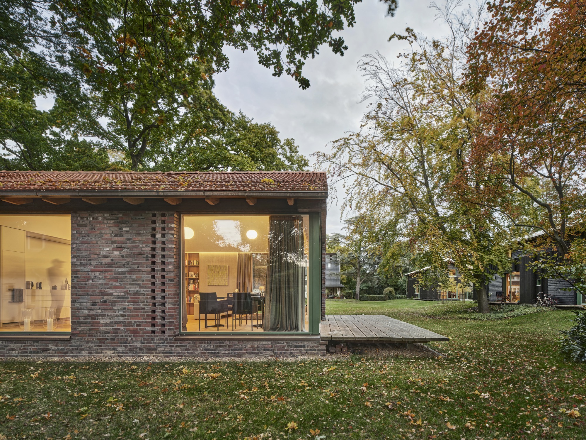 Perforated brick facade and corner glazing beneath a clay tile roof at dusk