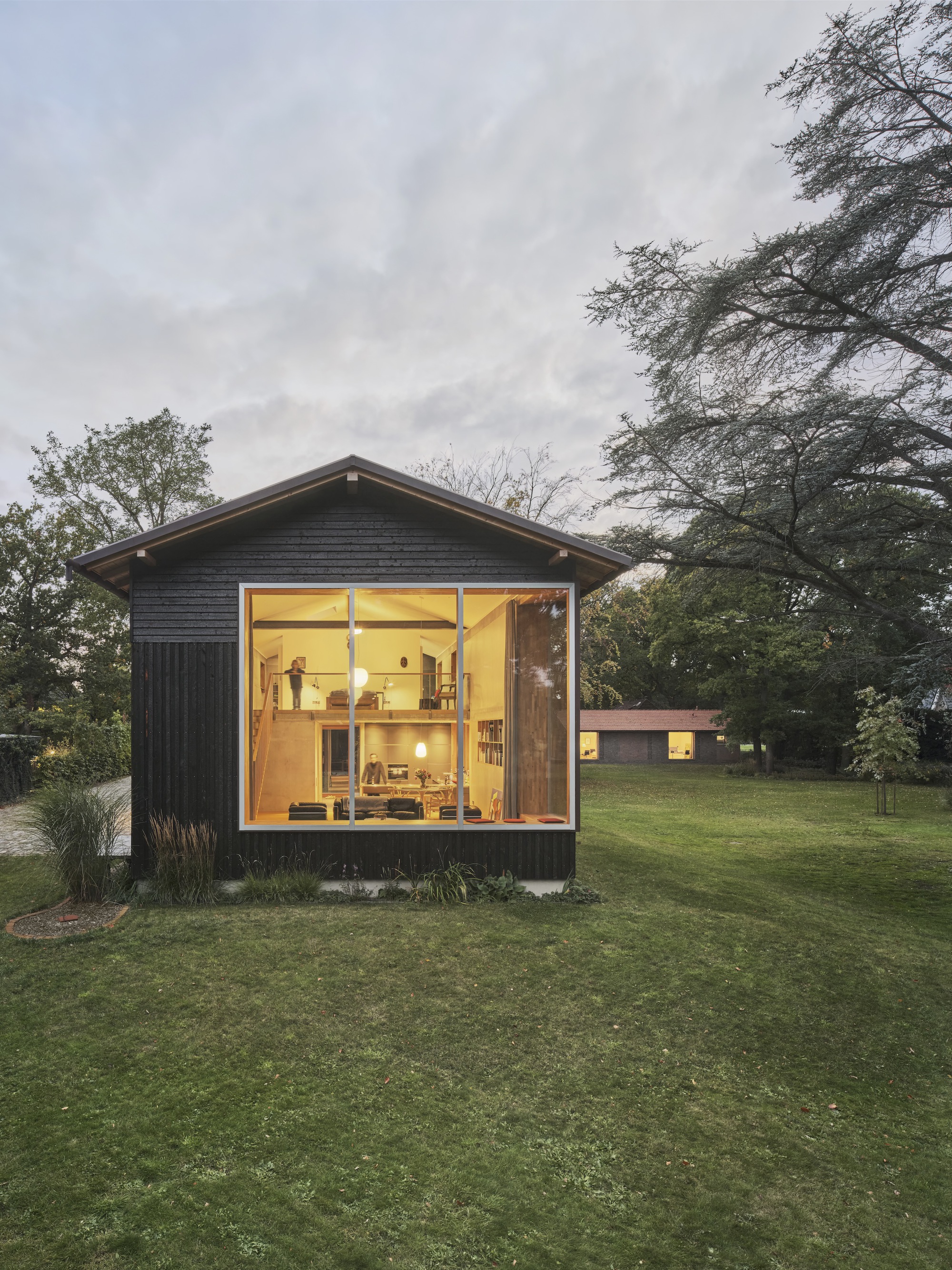 Gabled studio volume with full-height glazing and dark timber cladding at twilight