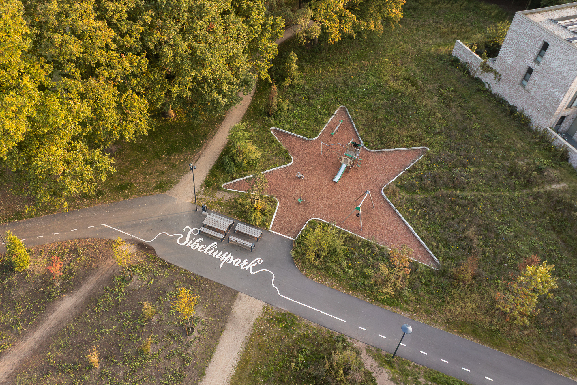 Overhead view of a star-shaped red rubber playground surface bordered with white edging and play equipment