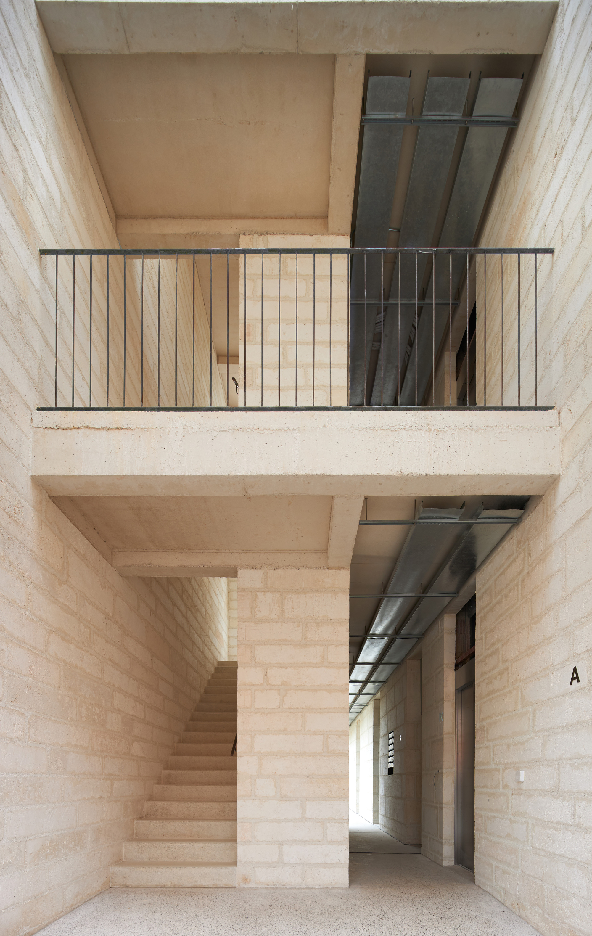 Internal stairwell with pale stone walls, steel balcony railings and glass block windows across two levels