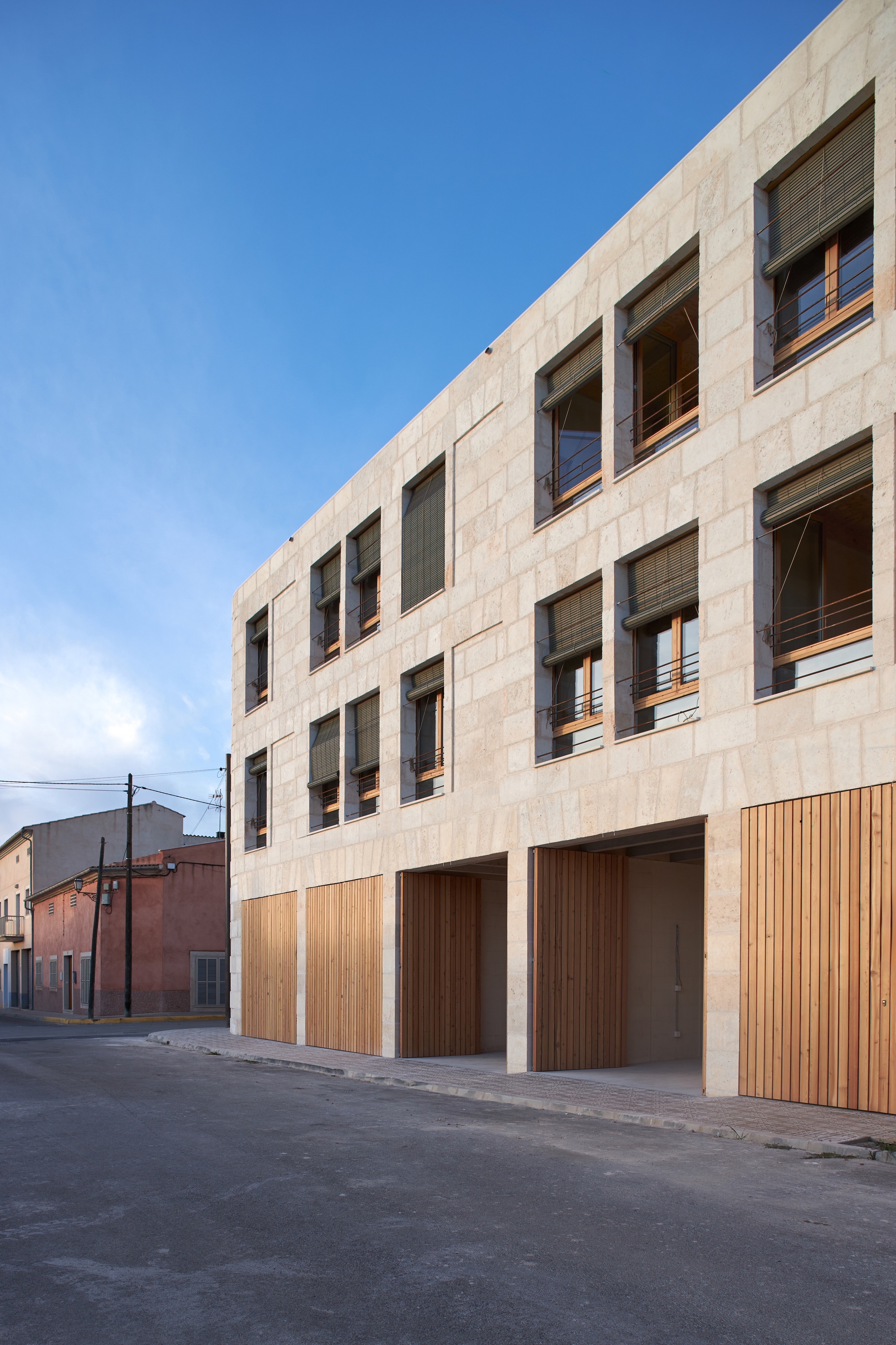 Street-facing facade with vertical timber garage doors beneath punched stone window openings