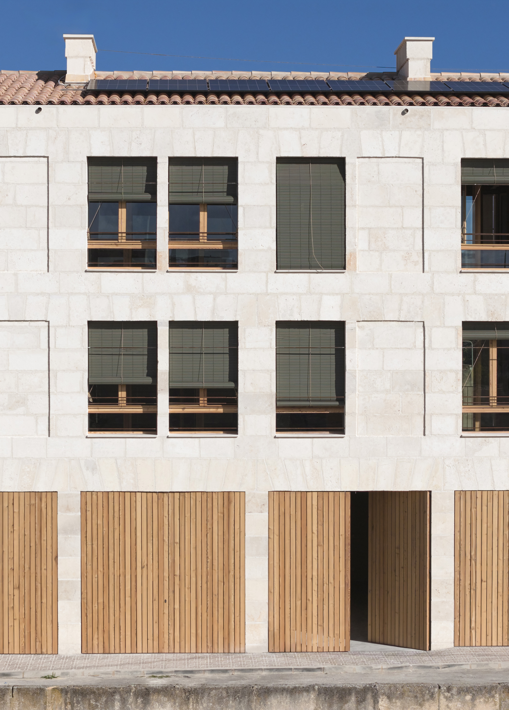 Ground level entry with timber slat doors and punched window openings in pale stone