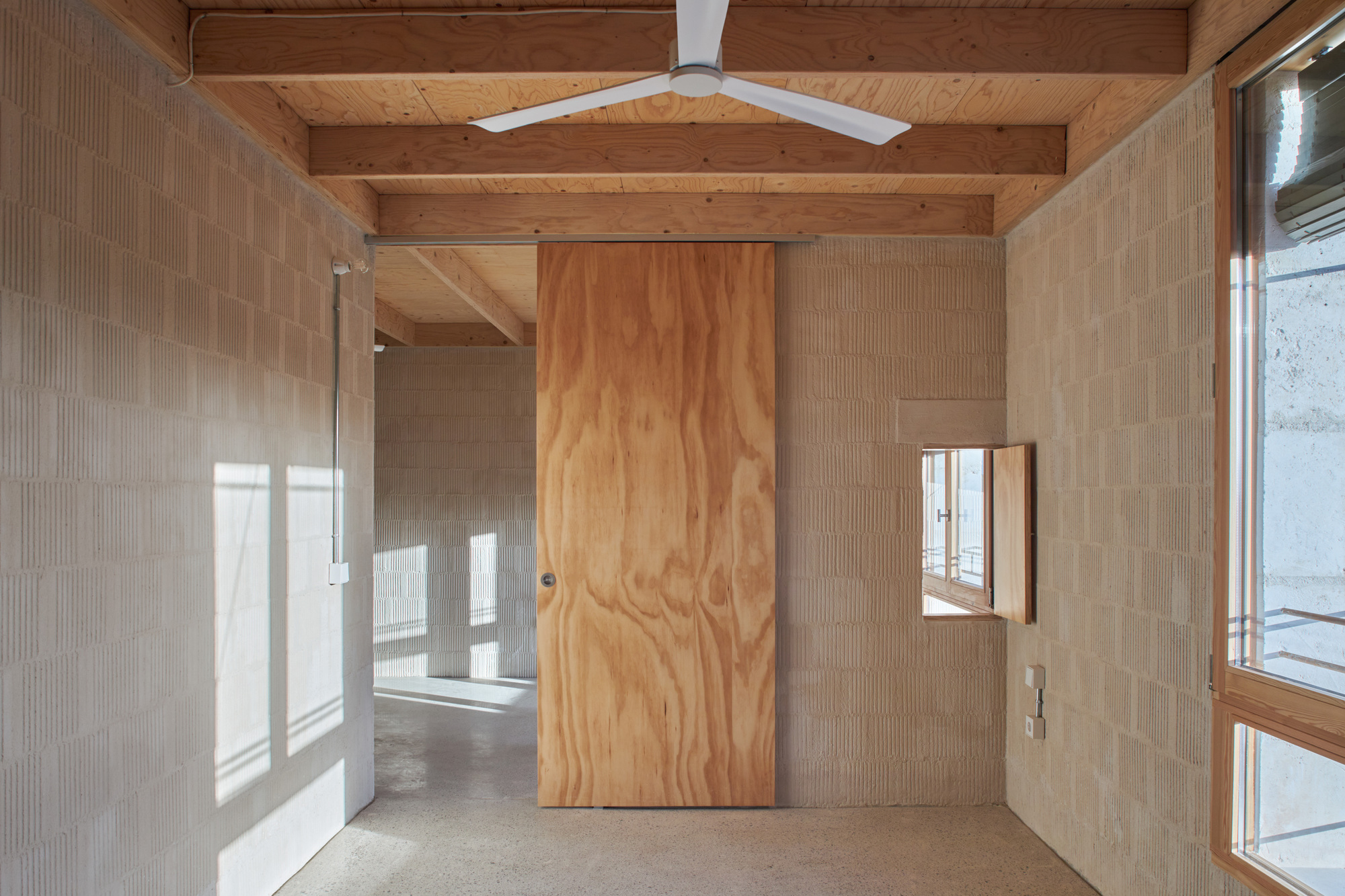 Large plywood sliding door set within a white ceramic tile wall beneath exposed timber beams with afternoon sunlight