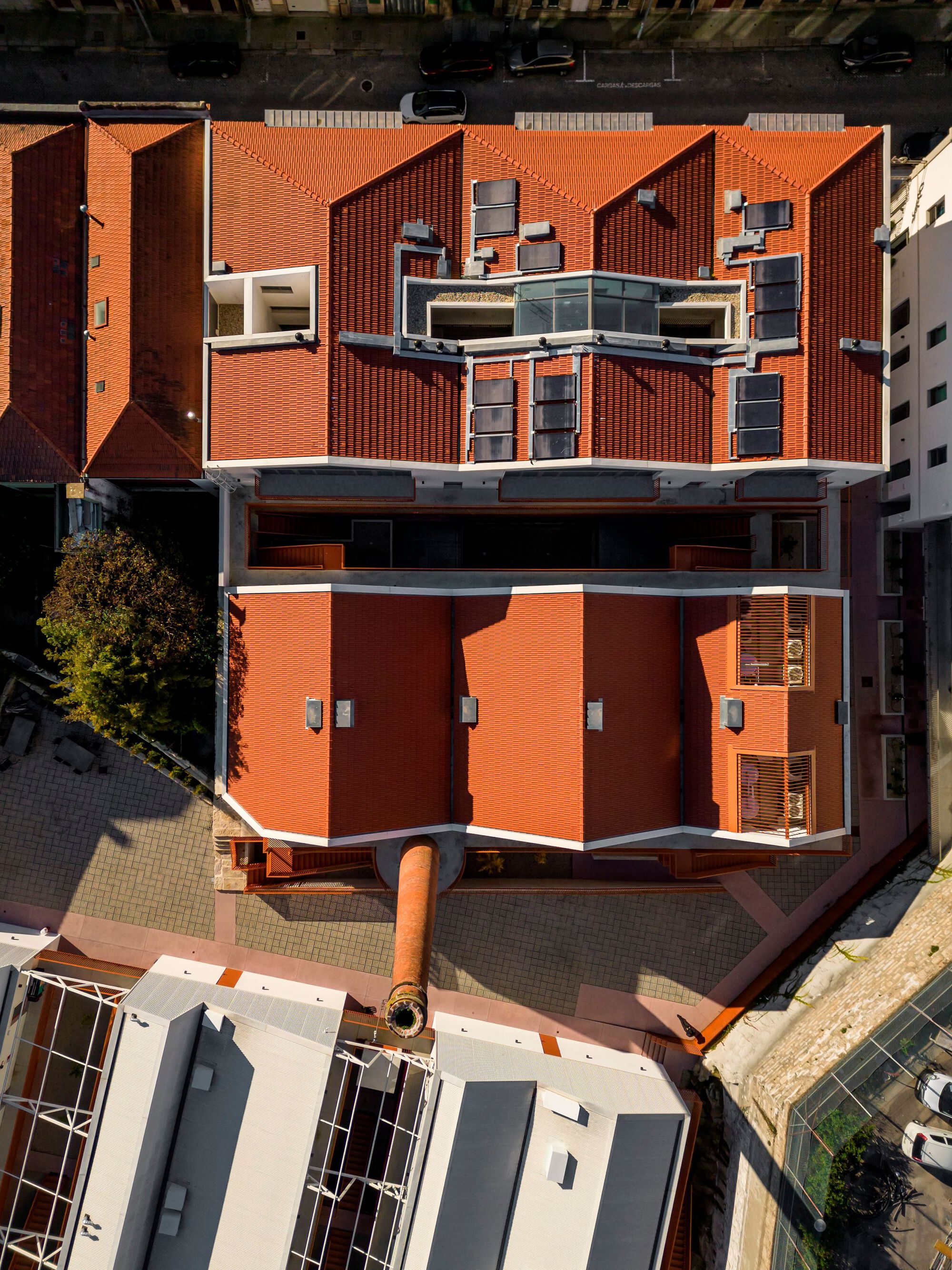 Top-down view of terraced roofscape with orange tile and cantilevered balconies overlooking neighboring buildings