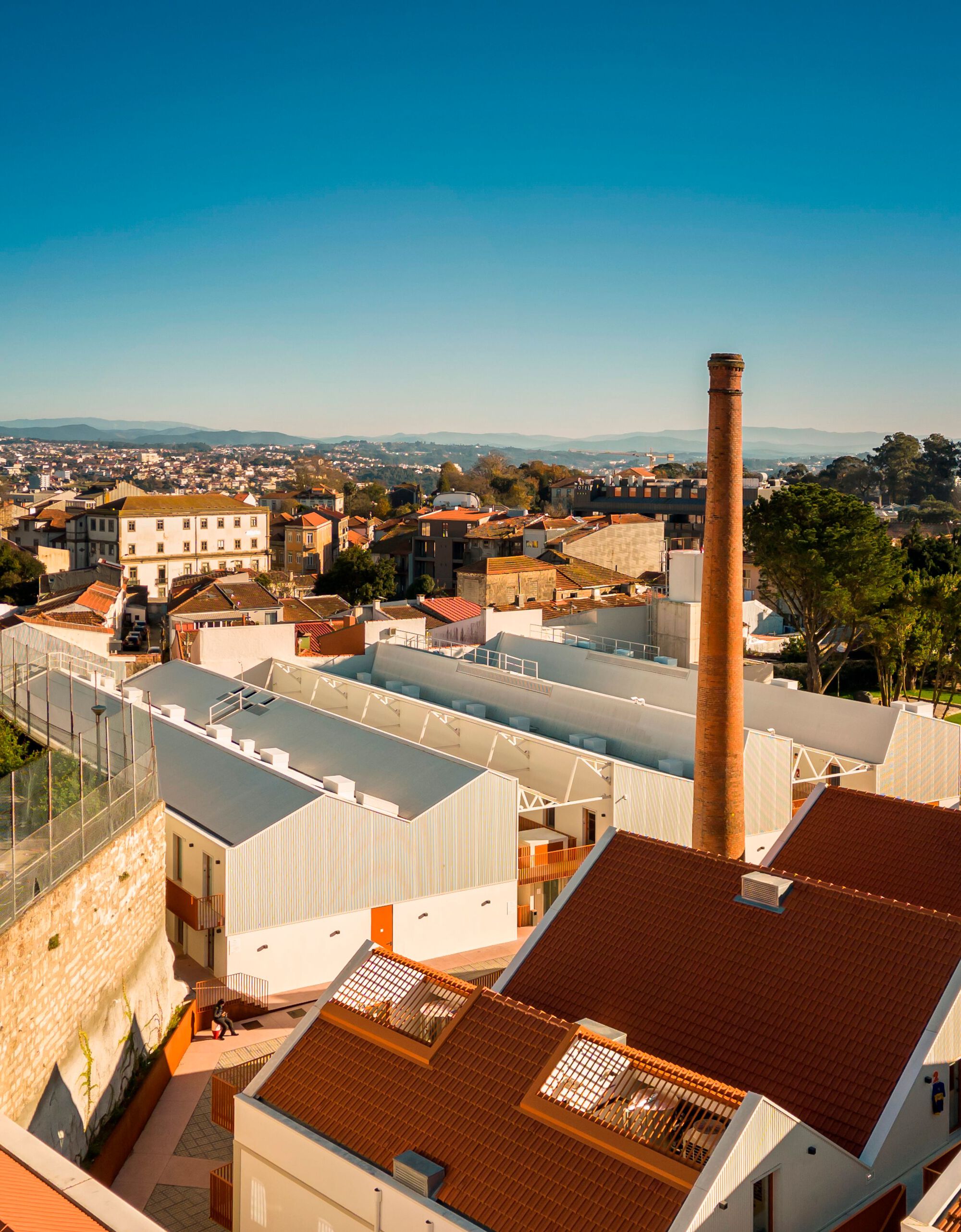 Elevated view of corrugated metal roofs with terracotta tiles and a tall brick chimney at sunset