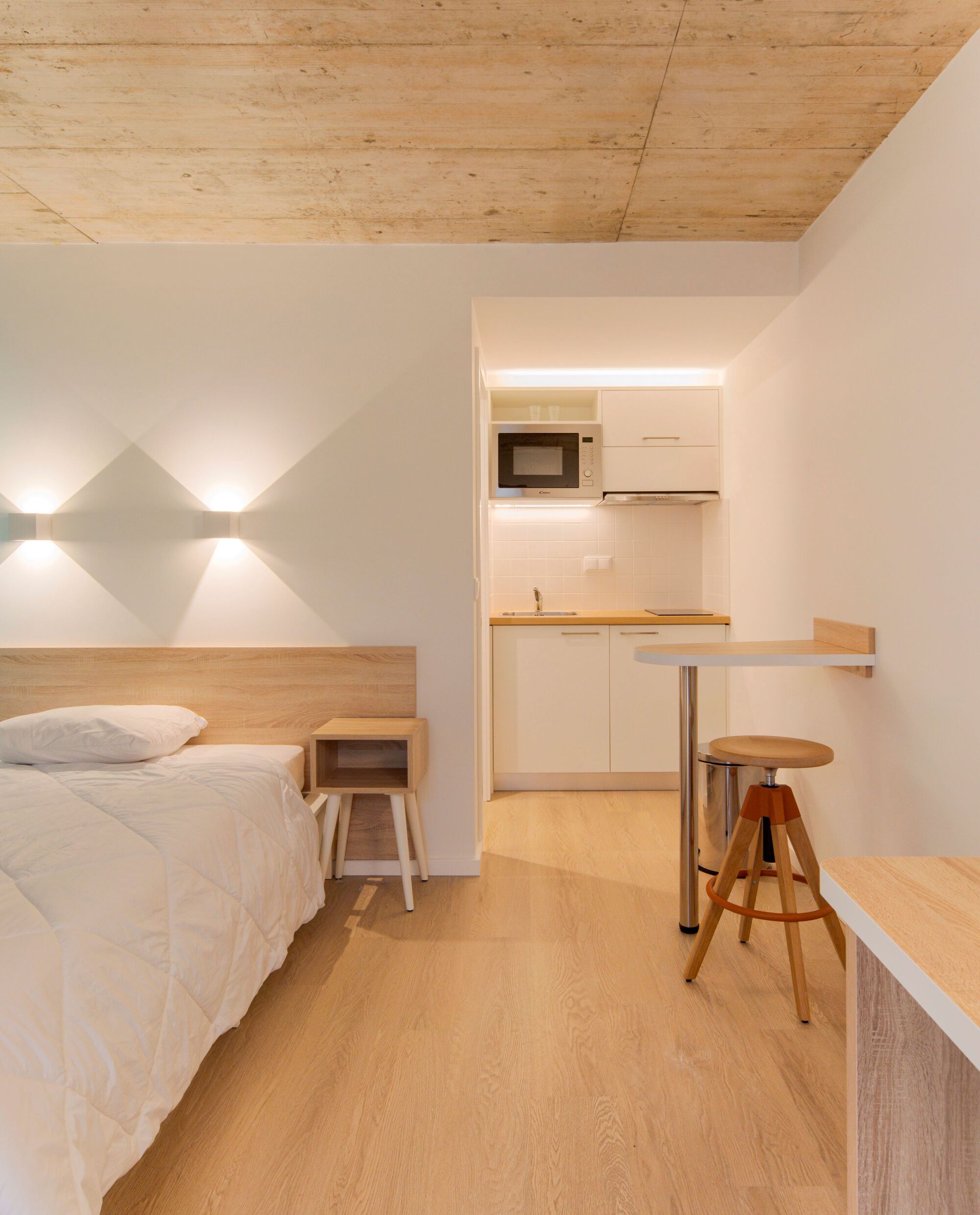 Compact sleeping unit with plywood ceiling and view through to the kitchenette alcove