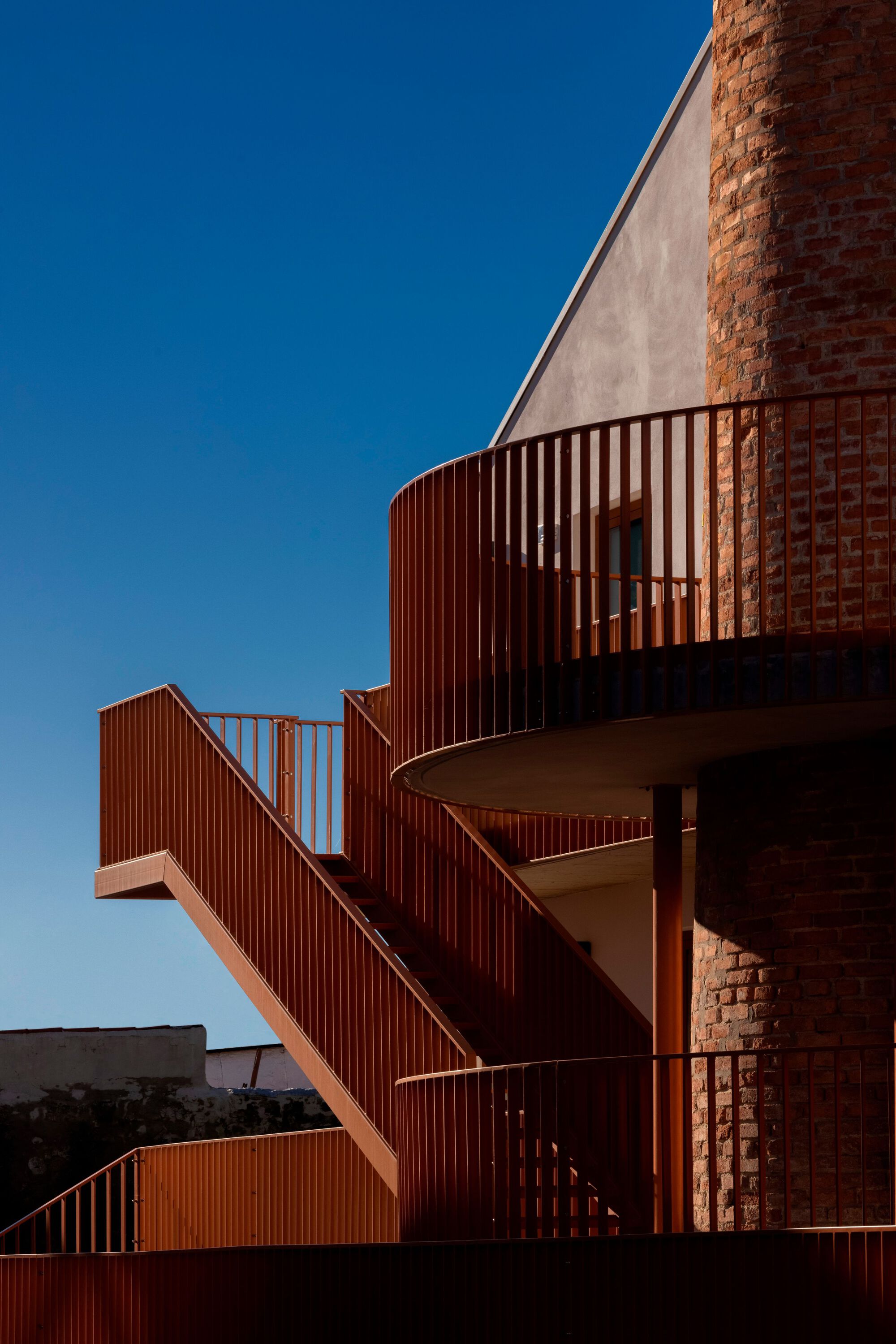Curved orange steel staircase wrapping around exposed brick chimney at dusk