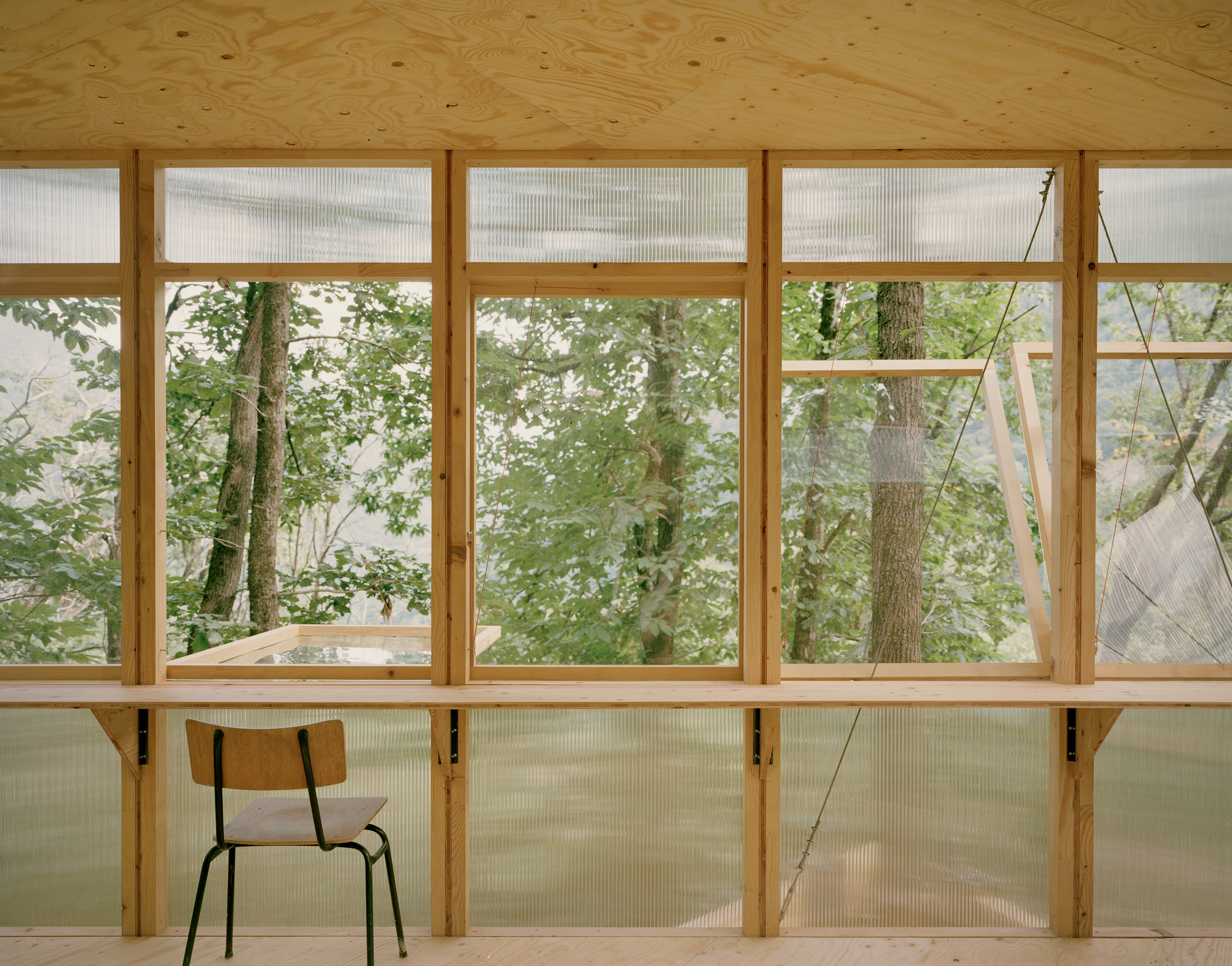 Interior wall with timber framing, translucent lower panels and clear upper glazing facing the forest