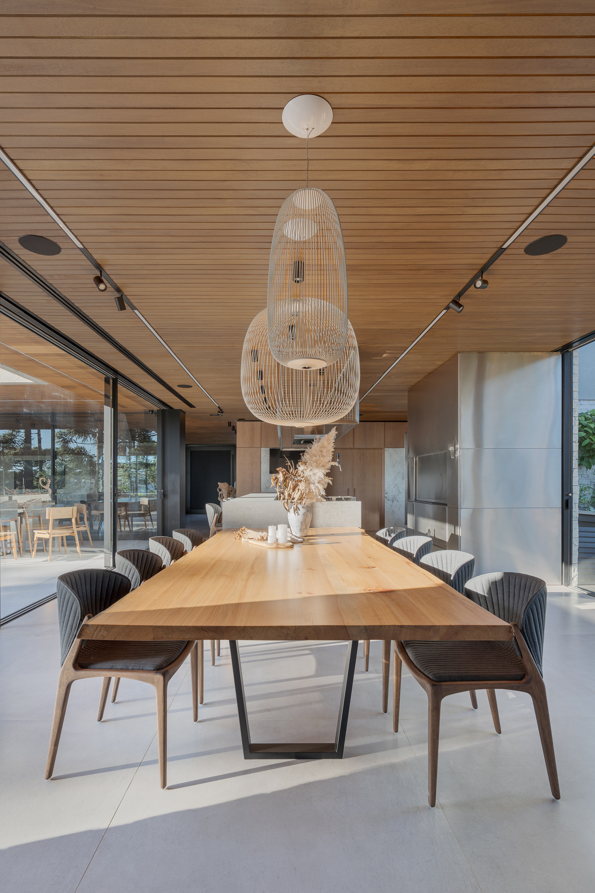 Dining table with pendant light fixture centered beneath continuous slatted wood ceiling and track lighting