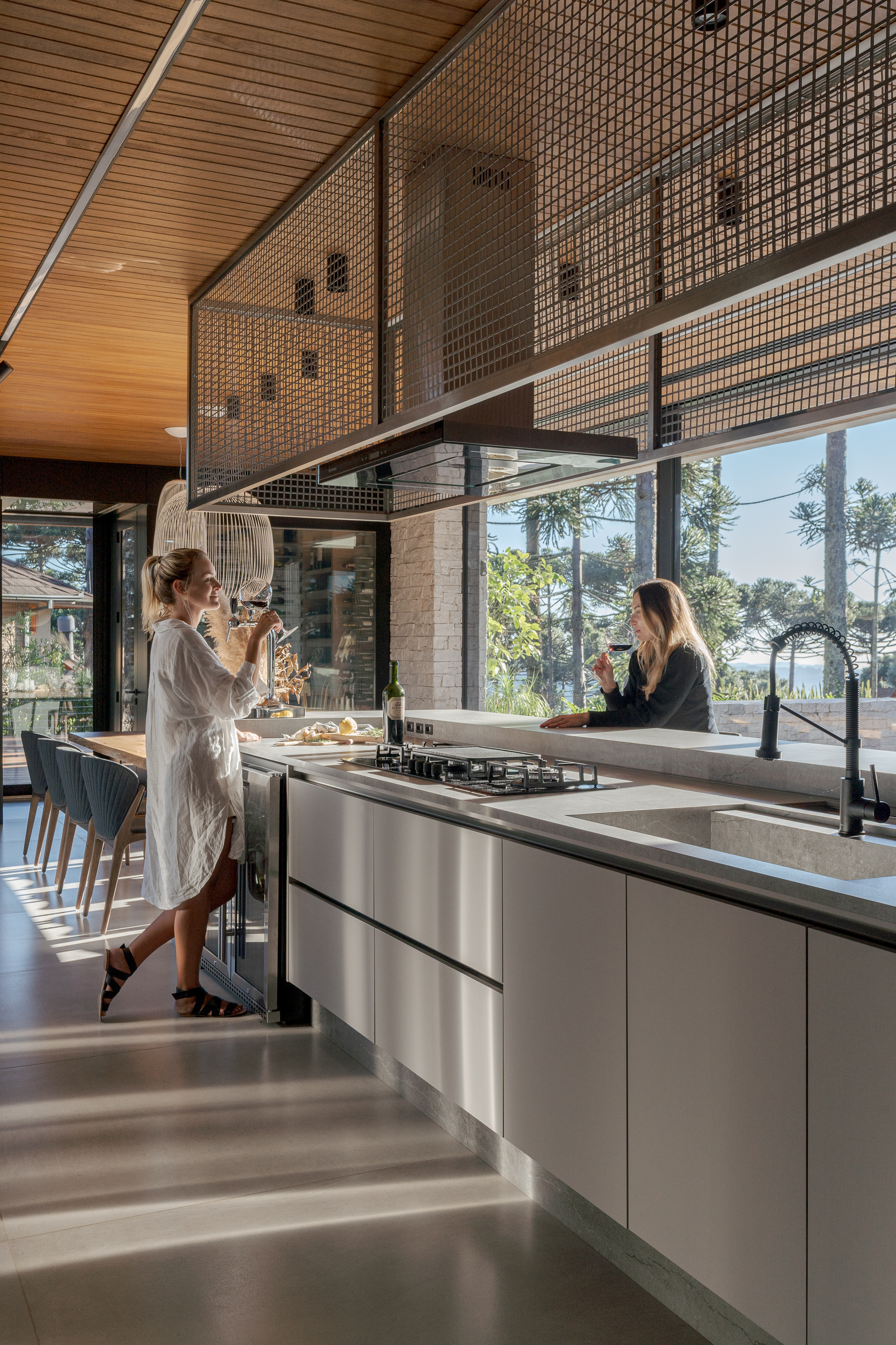 Kitchen island with two people preparing food beneath suspended mesh screen and glazed facade