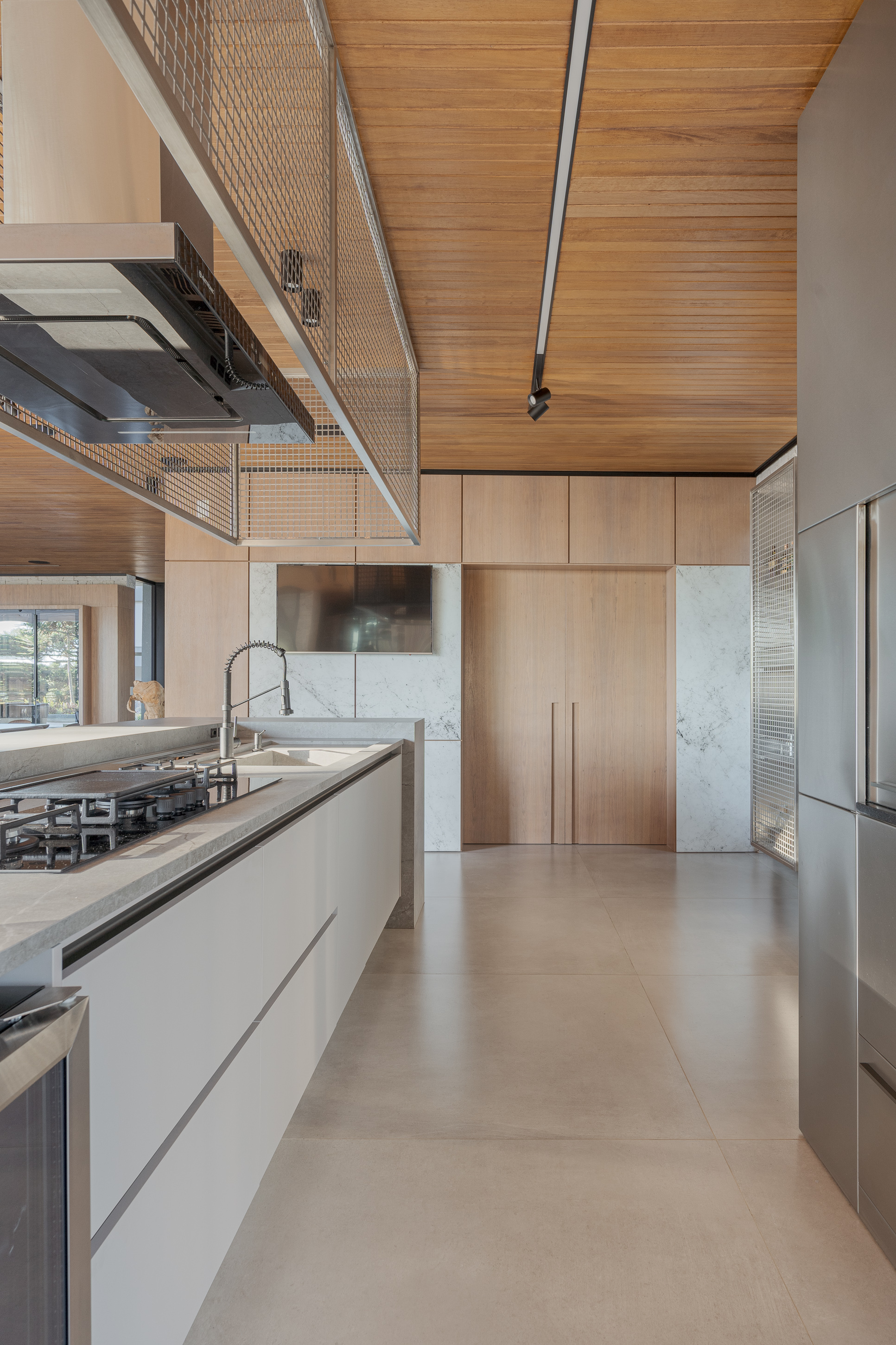 Double-height kitchen with wood-paneled ceiling, metal mesh balustrade, and stone countertops under natural light