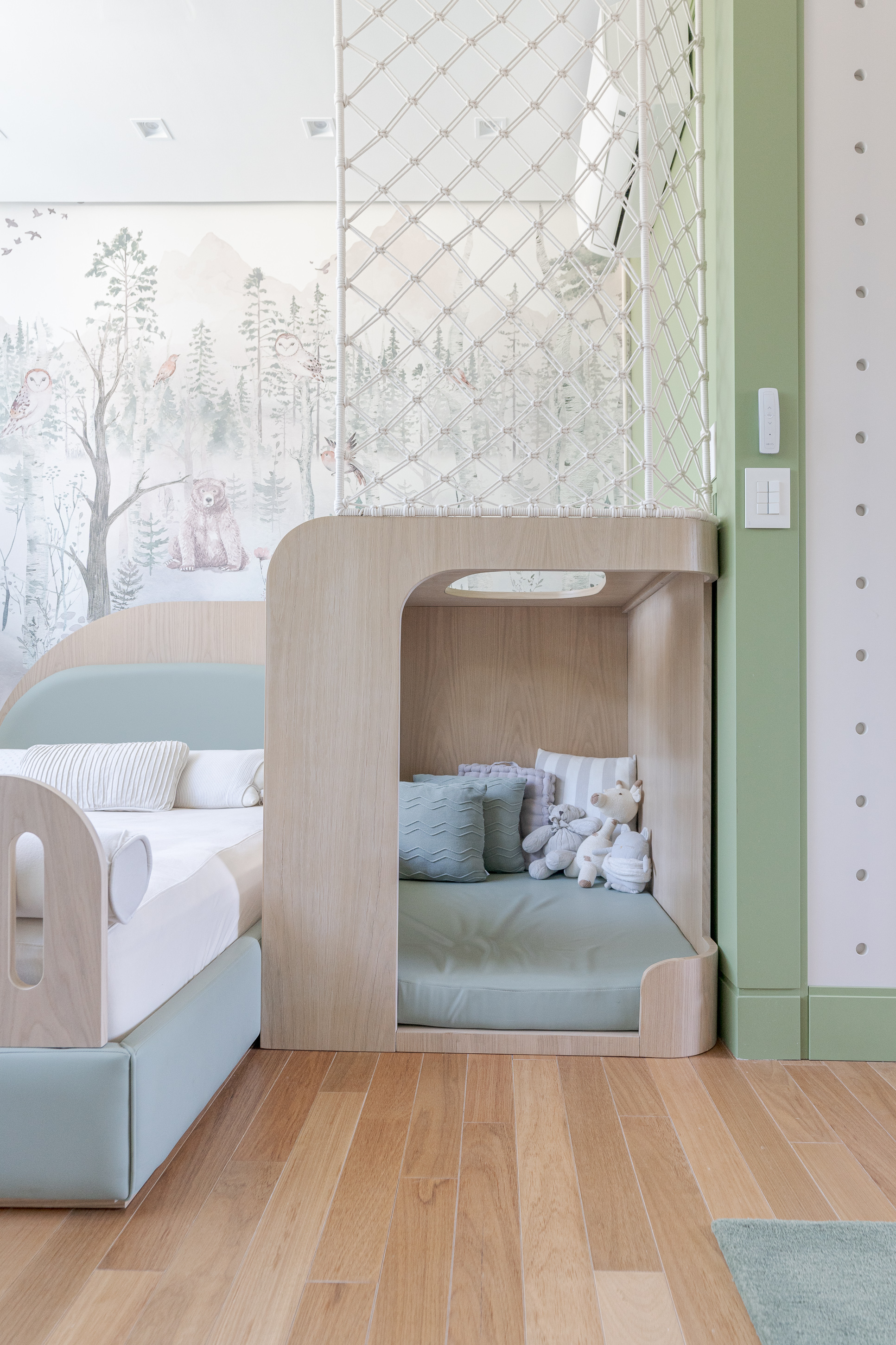 Curved timber play nook with built-in bed beneath wallpaper mural and mesh safety panel