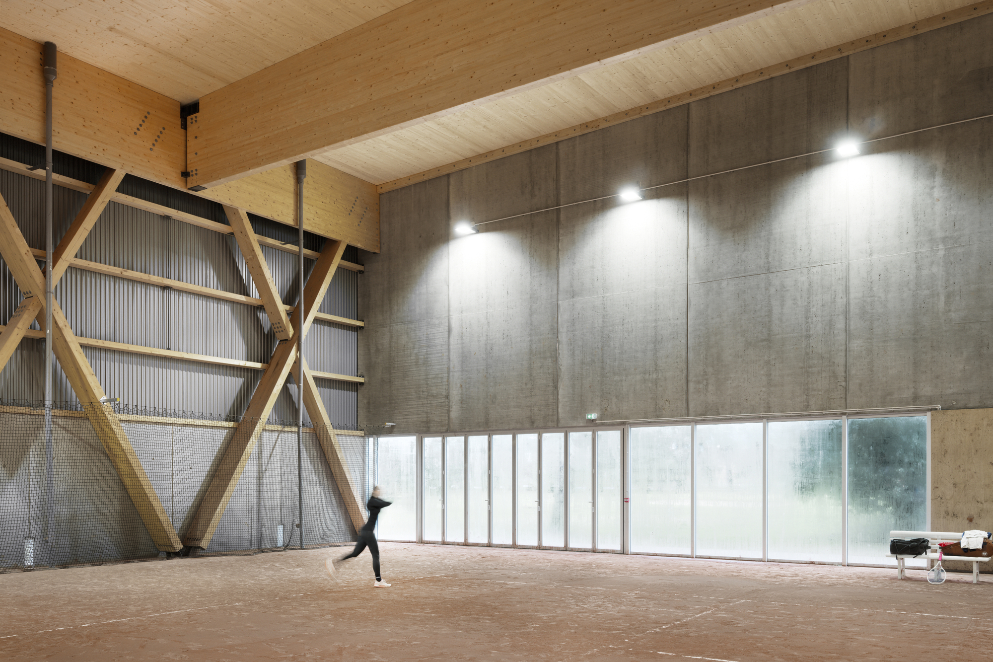 Interior hall with timber diagonal bracing and plywood ceiling as a figure walks across the clay floor