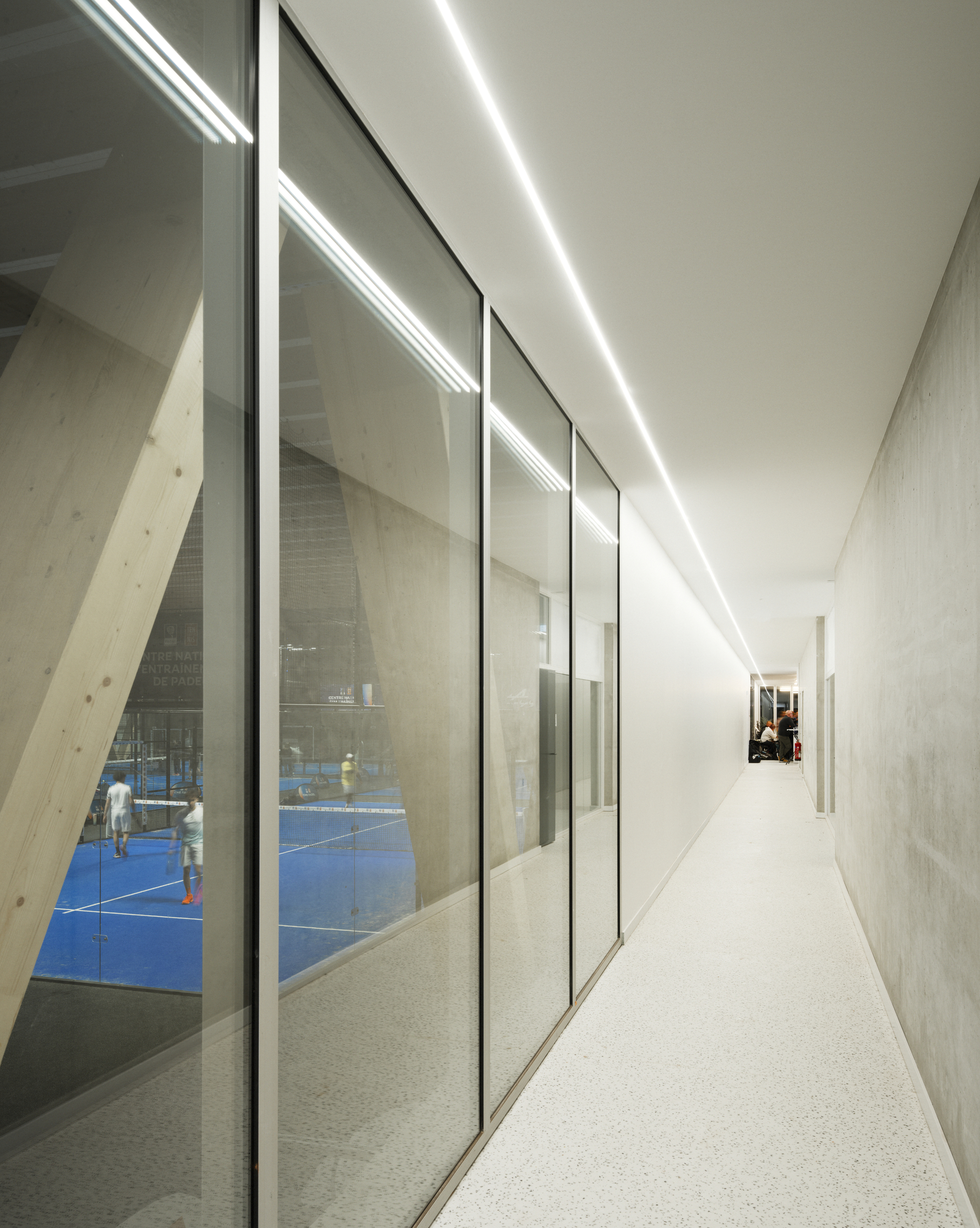 Corridor with angled glazing overlooking the indoor courts and recessed ceiling light strips