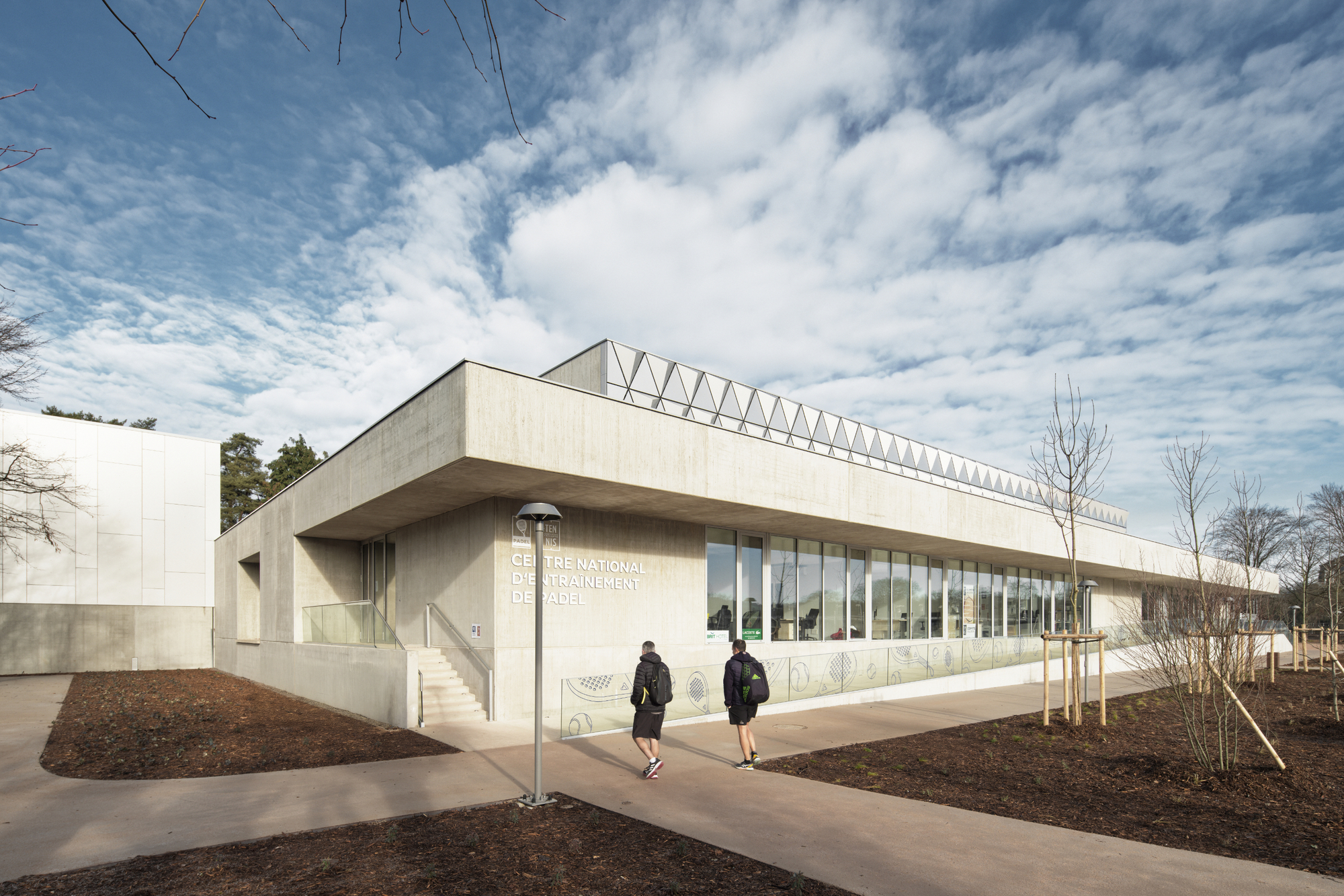 Entry facade with cantilevered roof overhang and two figures approaching on the paved path
