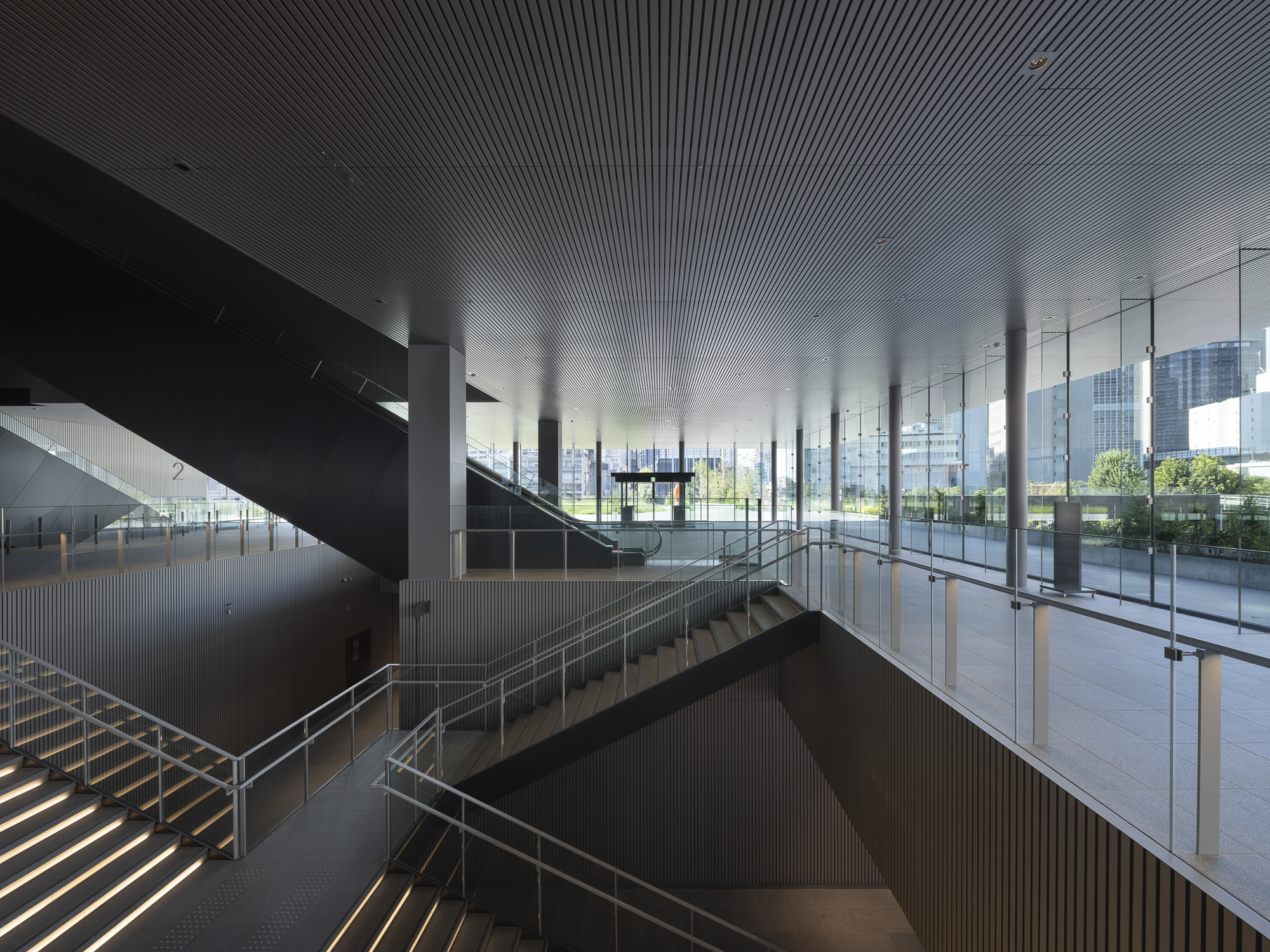 Interior atrium with intersecting black staircases beneath a ribbed ceiling with floor-to-ceiling glazing beyond
