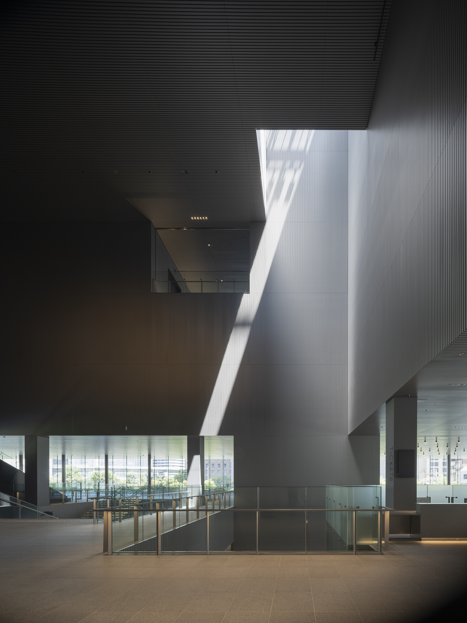 Double-height atrium with tilted ribbed wall catching sharp daylight from an overhead skylight