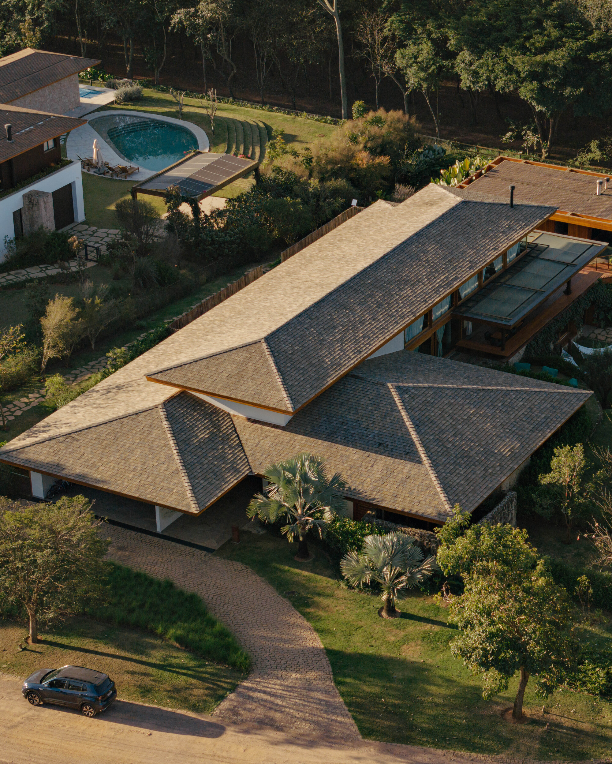 Aerial view of intersecting gable roofs with clay tiles and timber eaves among palm trees and lawn