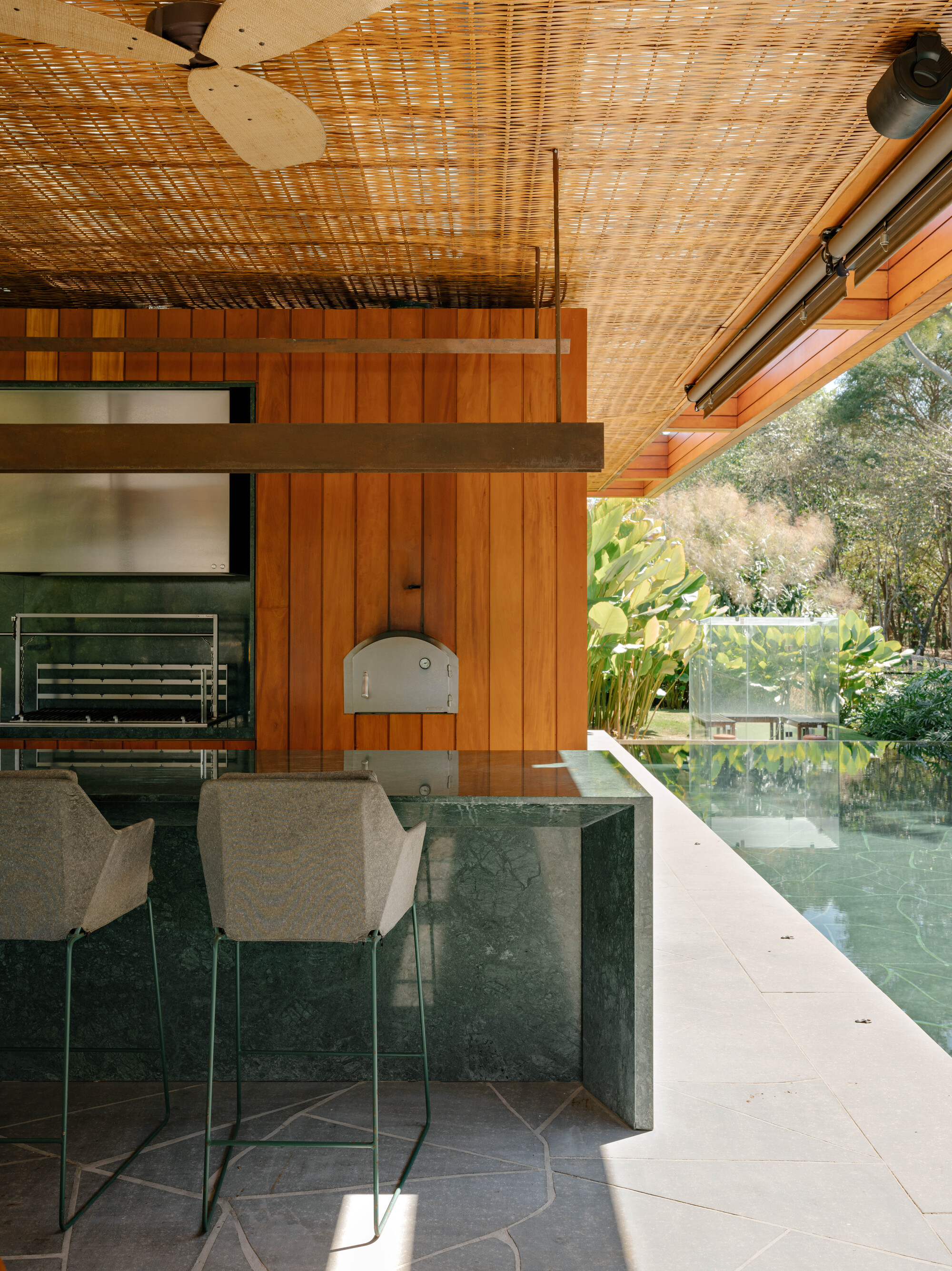 Kitchen counter with green marble base and timber wall beside reflecting pool edge at dusk