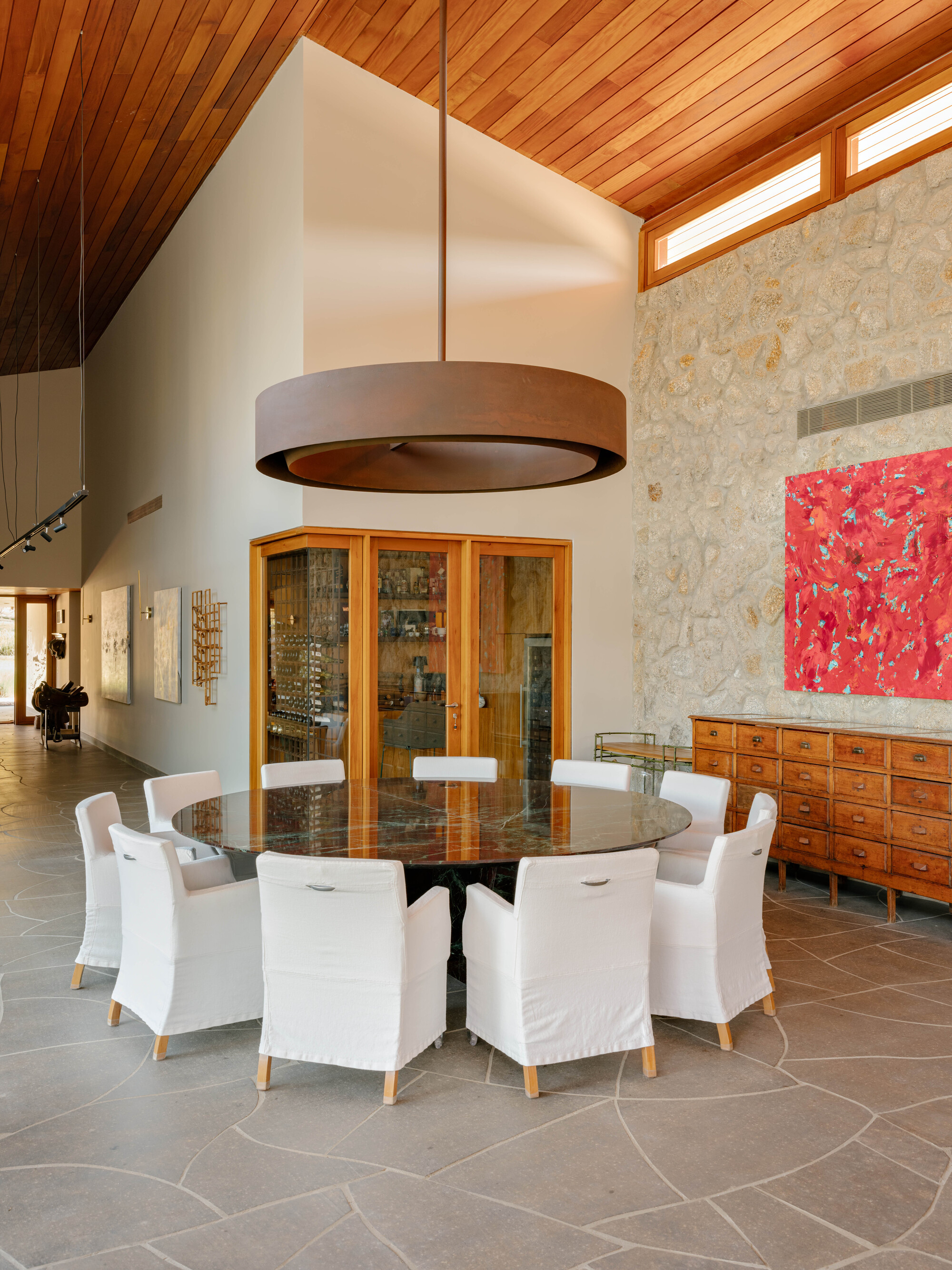 Dining area with circular drum pendant light above round table beneath vaulted timber ceiling and clerestory windows