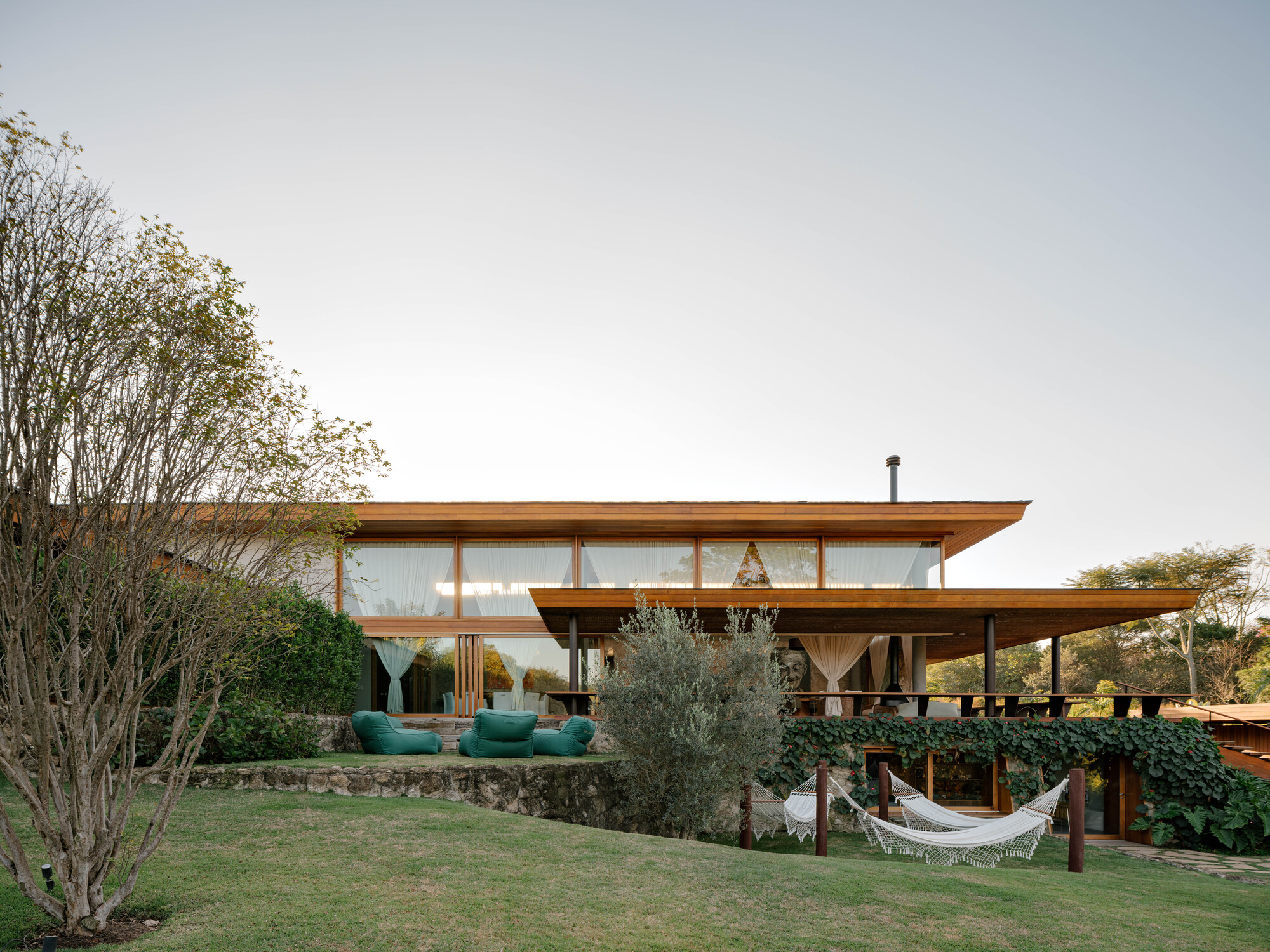 Garden view of the two-story timber residence with exposed beams and continuous glazing under overhanging roofs