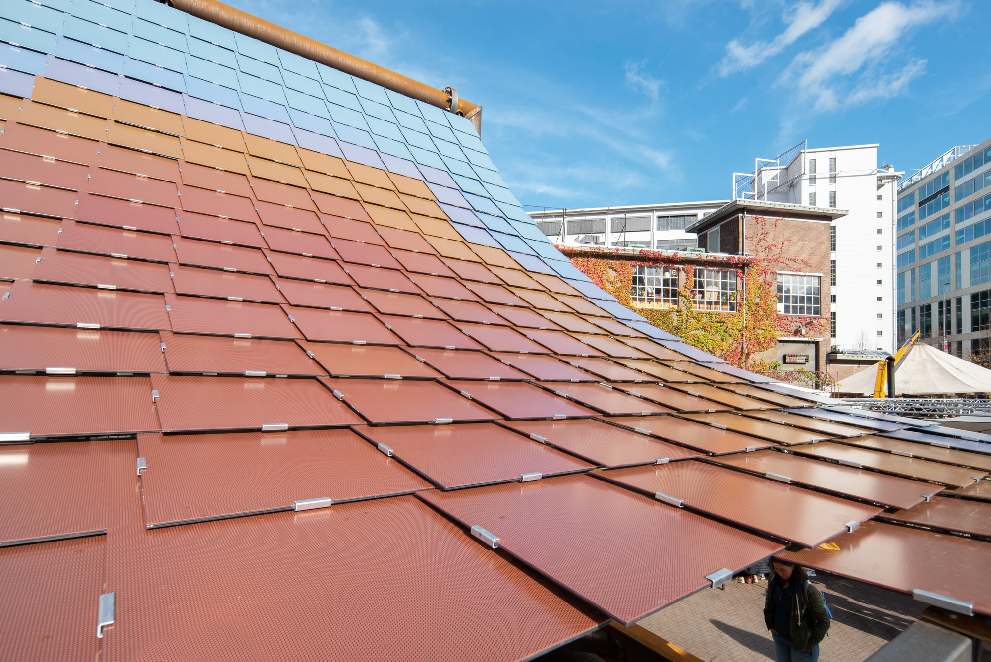 Close-up of the terracotta-toned solar panel array transitioning to blue panels with buildings visible beyond