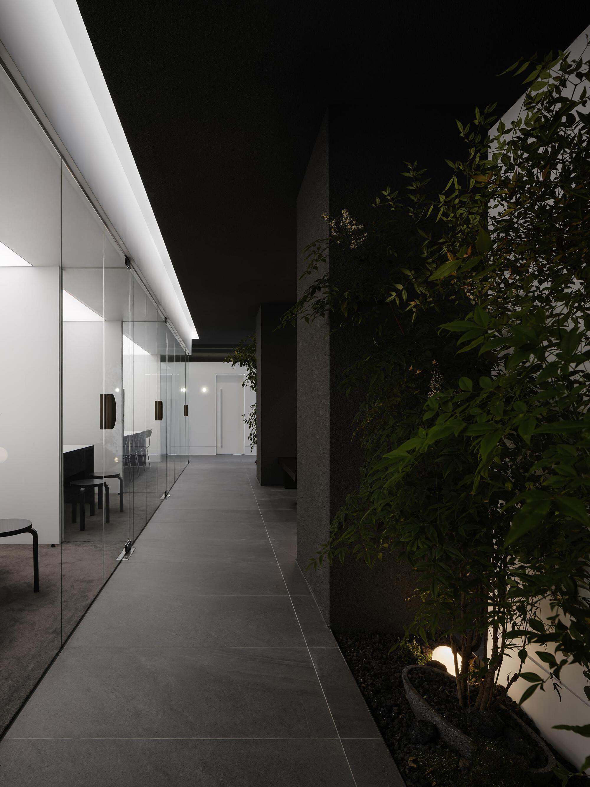 Evening corridor with uplights illuminating a planted green wall and a glazed office beyond