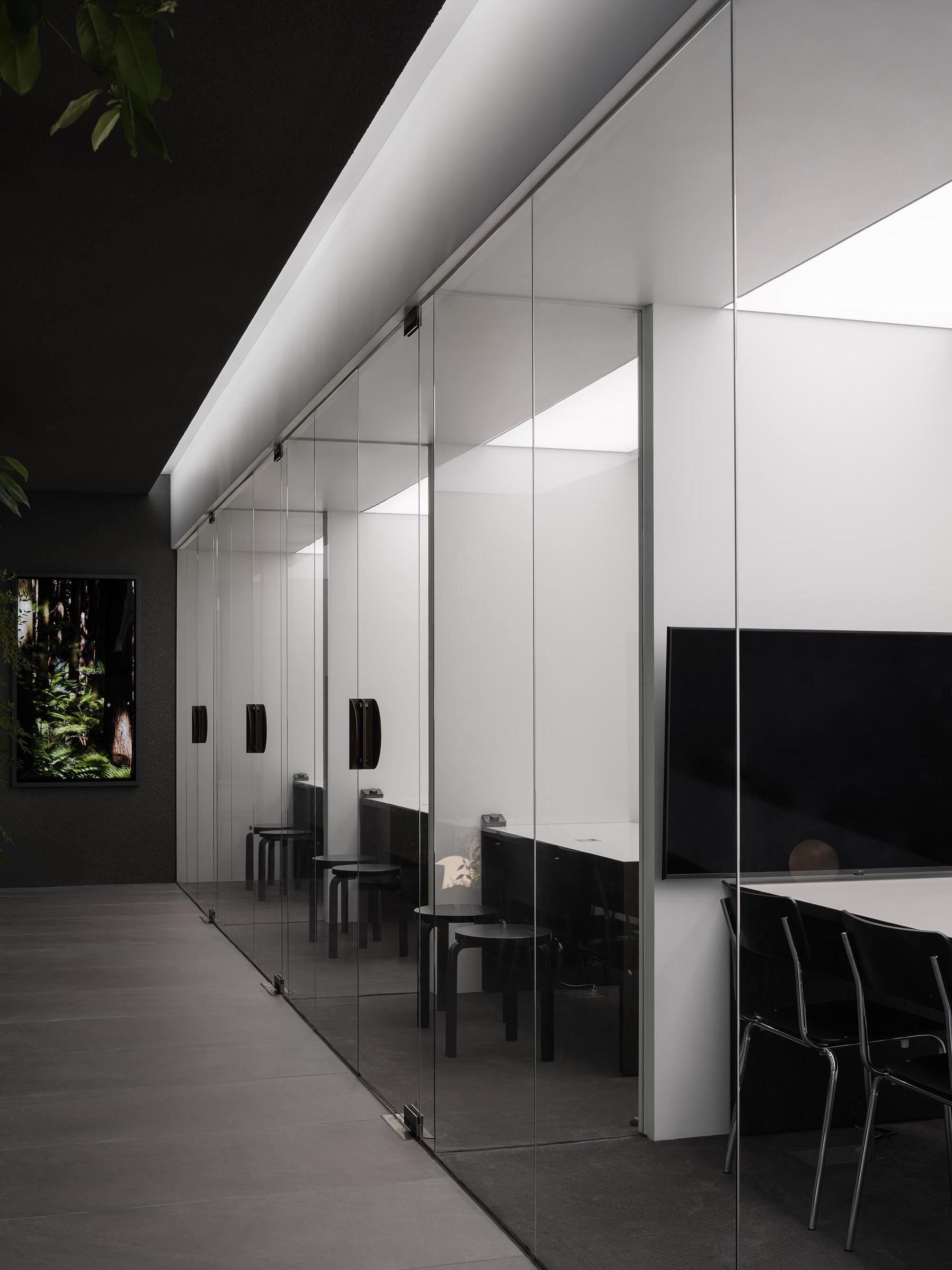 Full-height glass partition along the corridor with black-framed doors and uplighting under white soffit