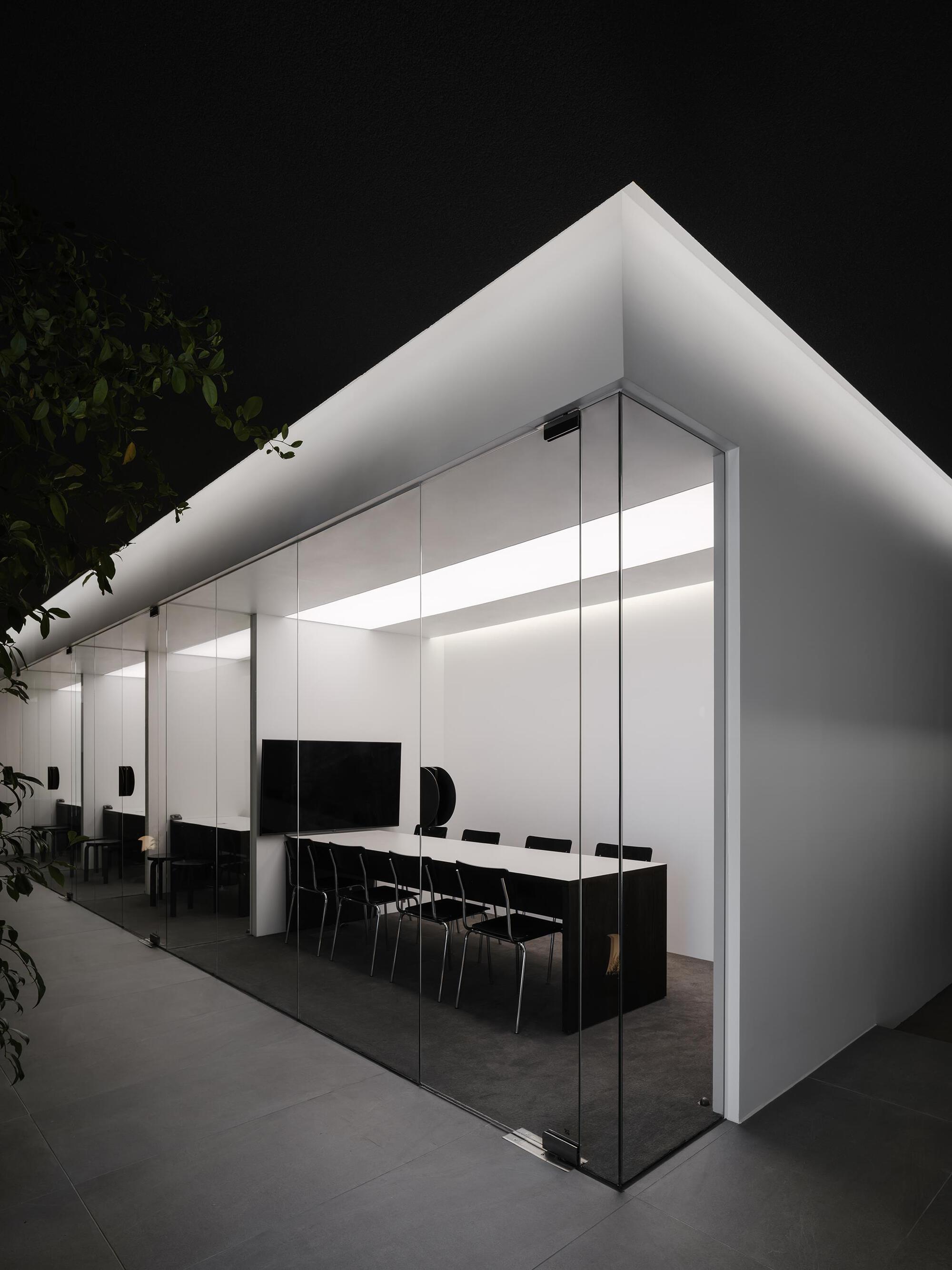 Glass-enclosed meeting room volume with continuous perimeter lighting glowing against the night sky